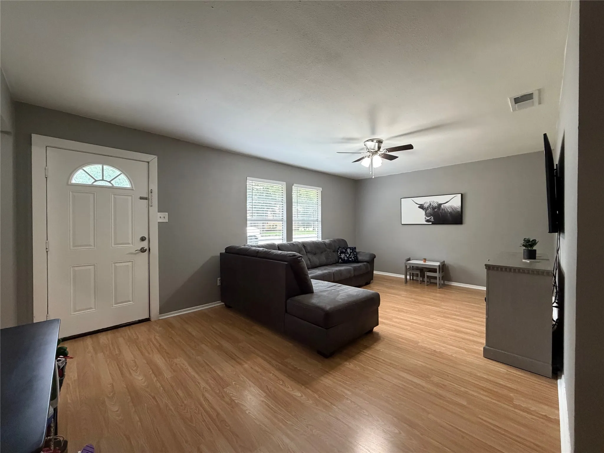 Spacious room featuring wood-finish flooring, neutral gray walls, and a ceiling fan with integrated lighting