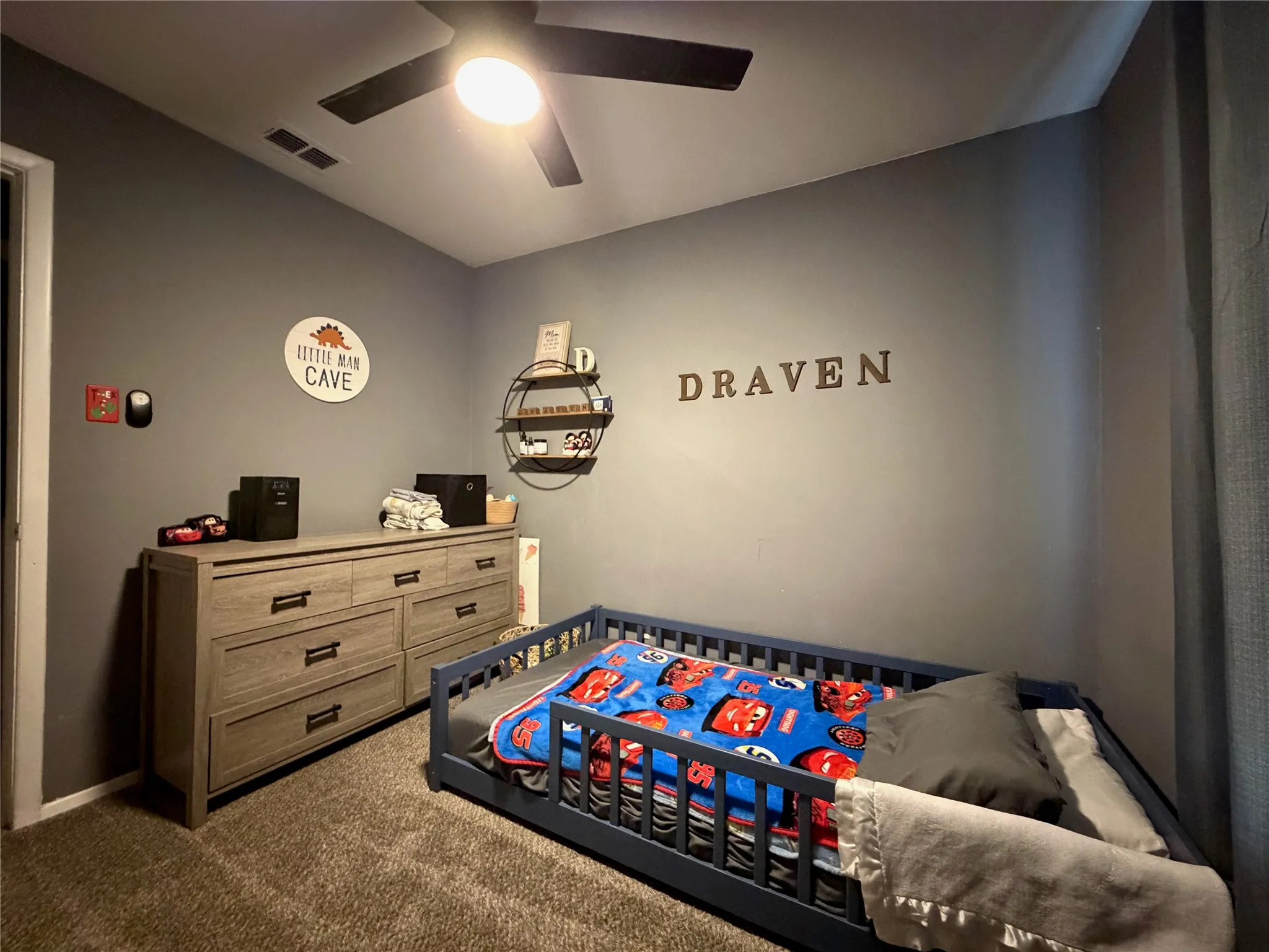 Room featuring a neutral wall color, dark ceiling fan with integrated lighting, and textured carpet flooring
