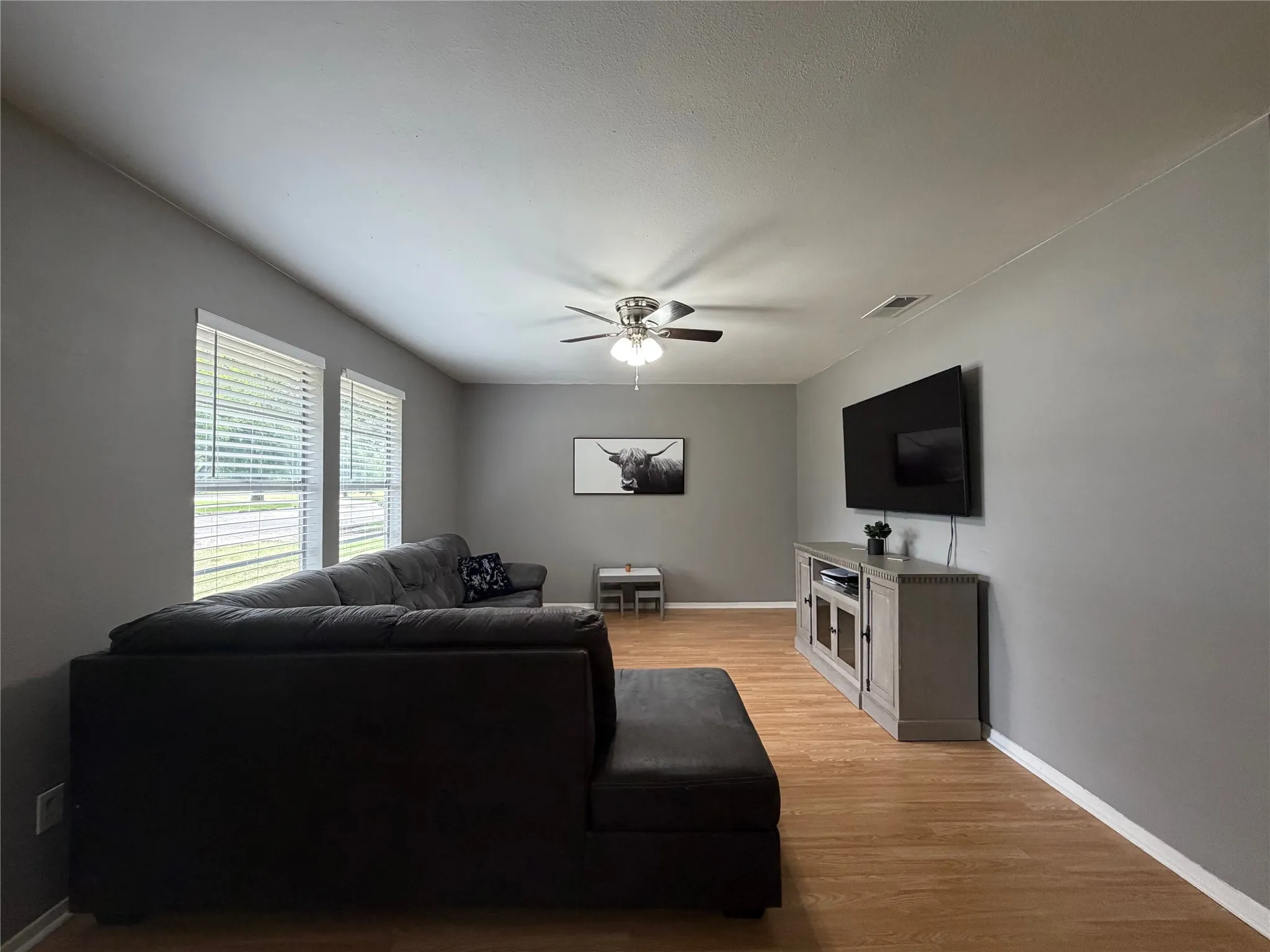Living area featuring wood-finish flooring, light grey walls, and a ceiling fan with integrated lighting