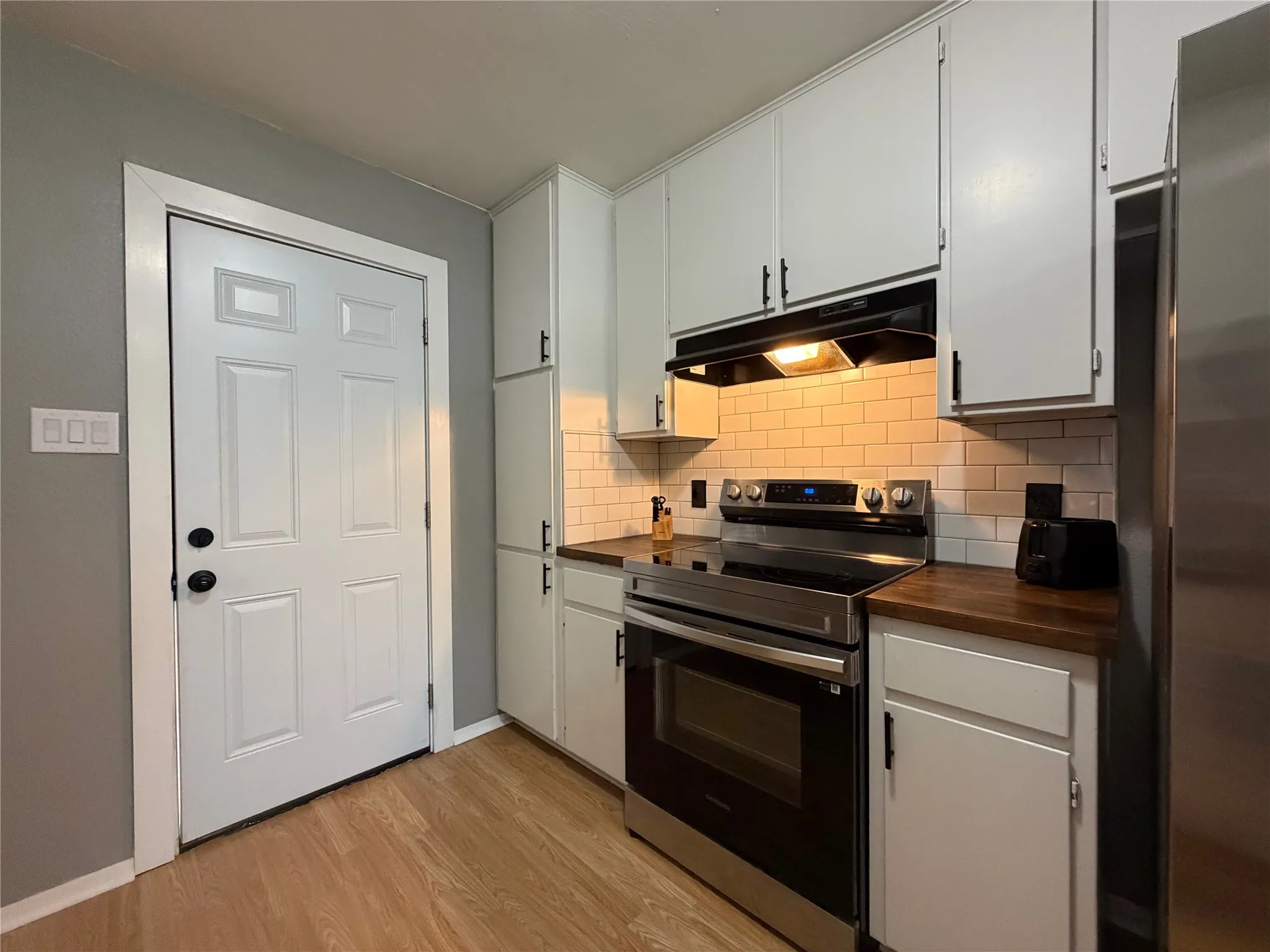 Kitchen featuring wood-finish flooring, white cabinetry with black hardware, subway tile backsplash, stainless steel range, and wood-finish countertops