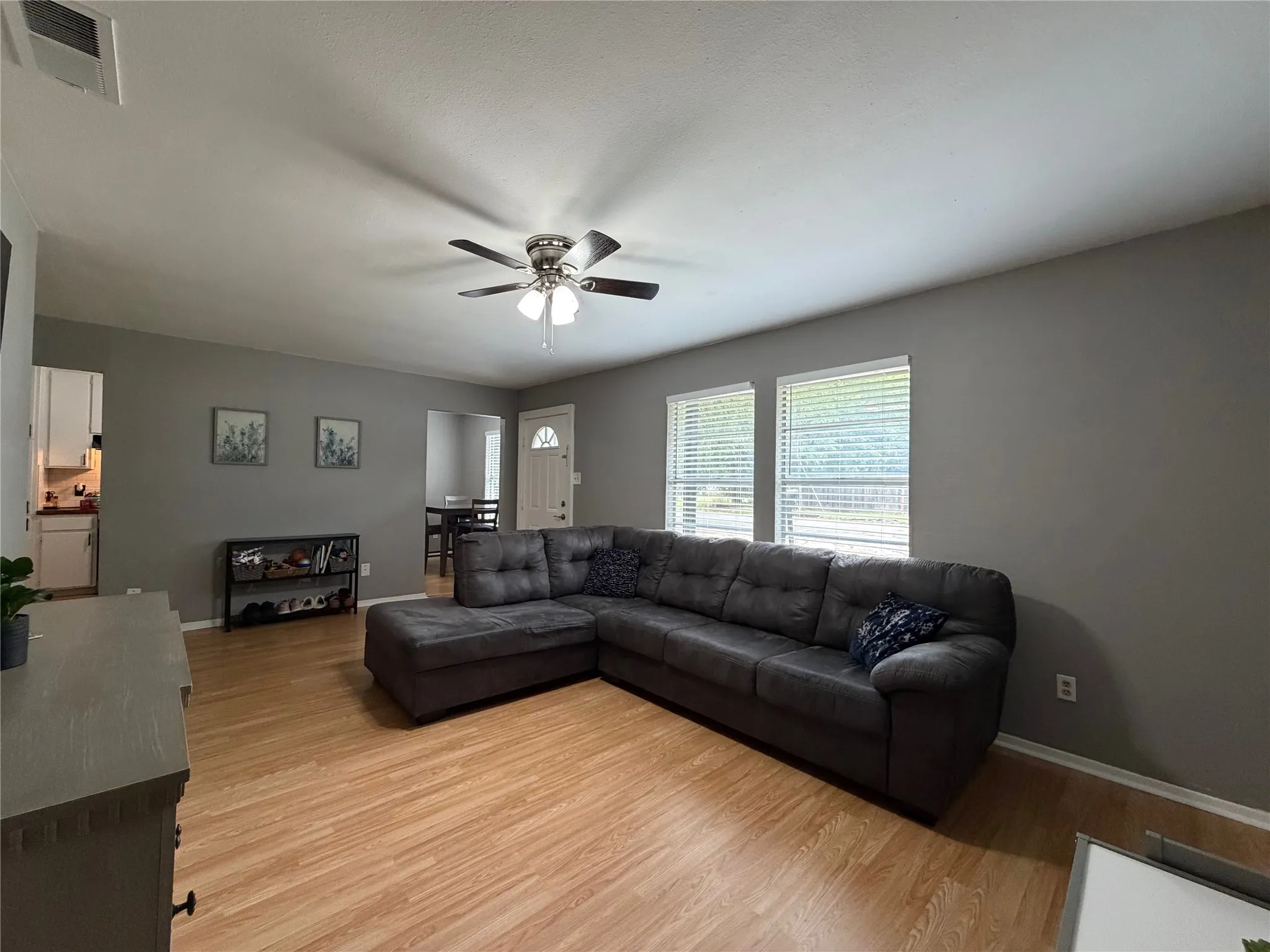 Spacious living area featuring wood-finish flooring, two large windows with blinds, and a ceiling fan with integrated lighting