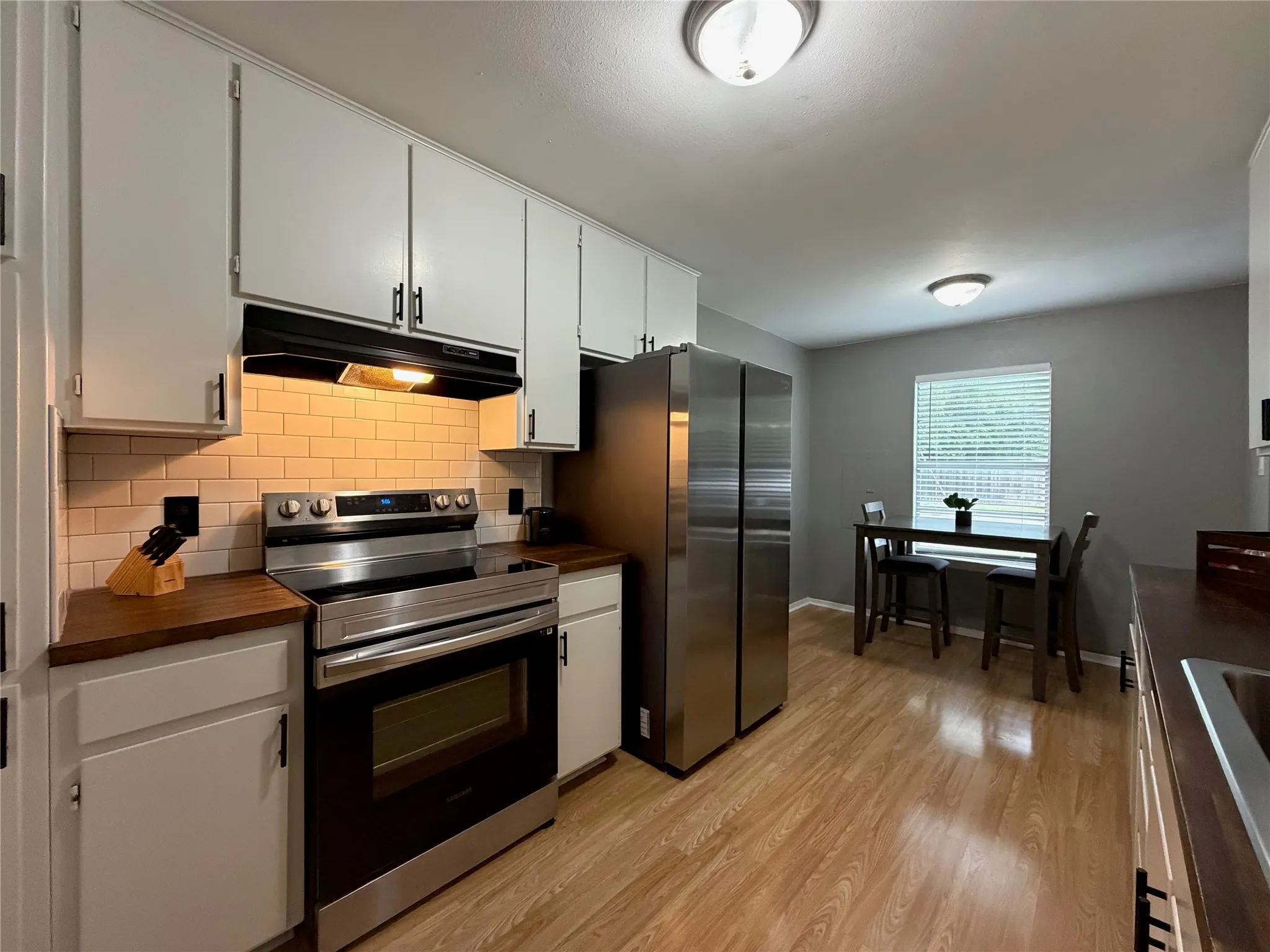 Kitchen featuring wood-finish flooring, white cabinetry with dark hardware, butcher block countertops, subway tile backsplash, and stainless steel appliances