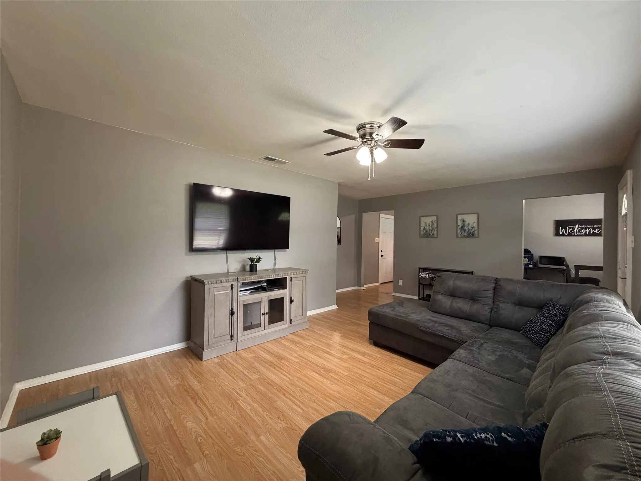 Open-concept living area featuring wood-finish flooring, a ceiling fan with integrated lighting, and neutral wall tones