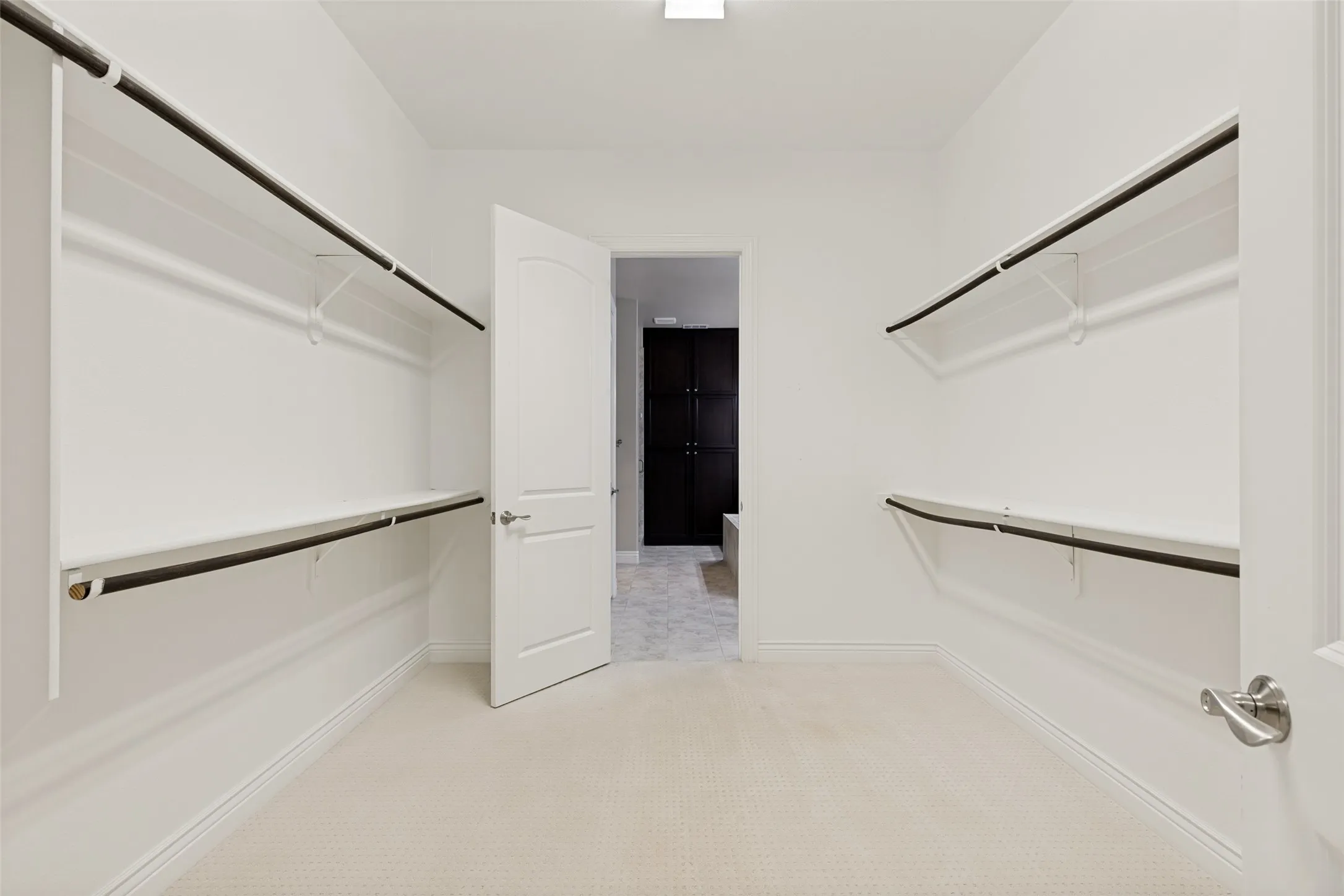 Walk-in closet featuring white shelving and chrome hanging rods