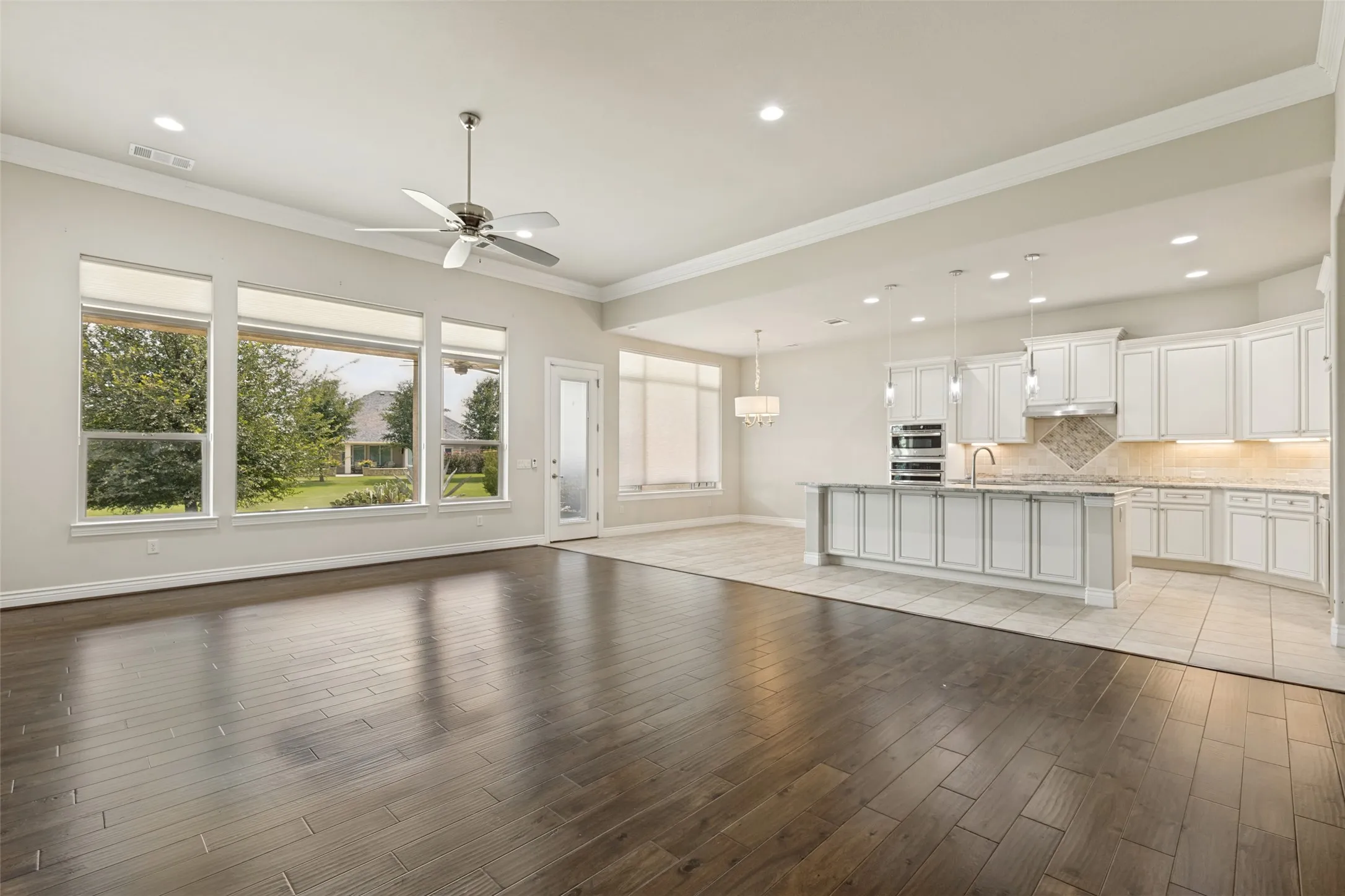 Open-concept living space featuring rich wood-finish flooring, a contemporary ceiling fan, and large picture windows