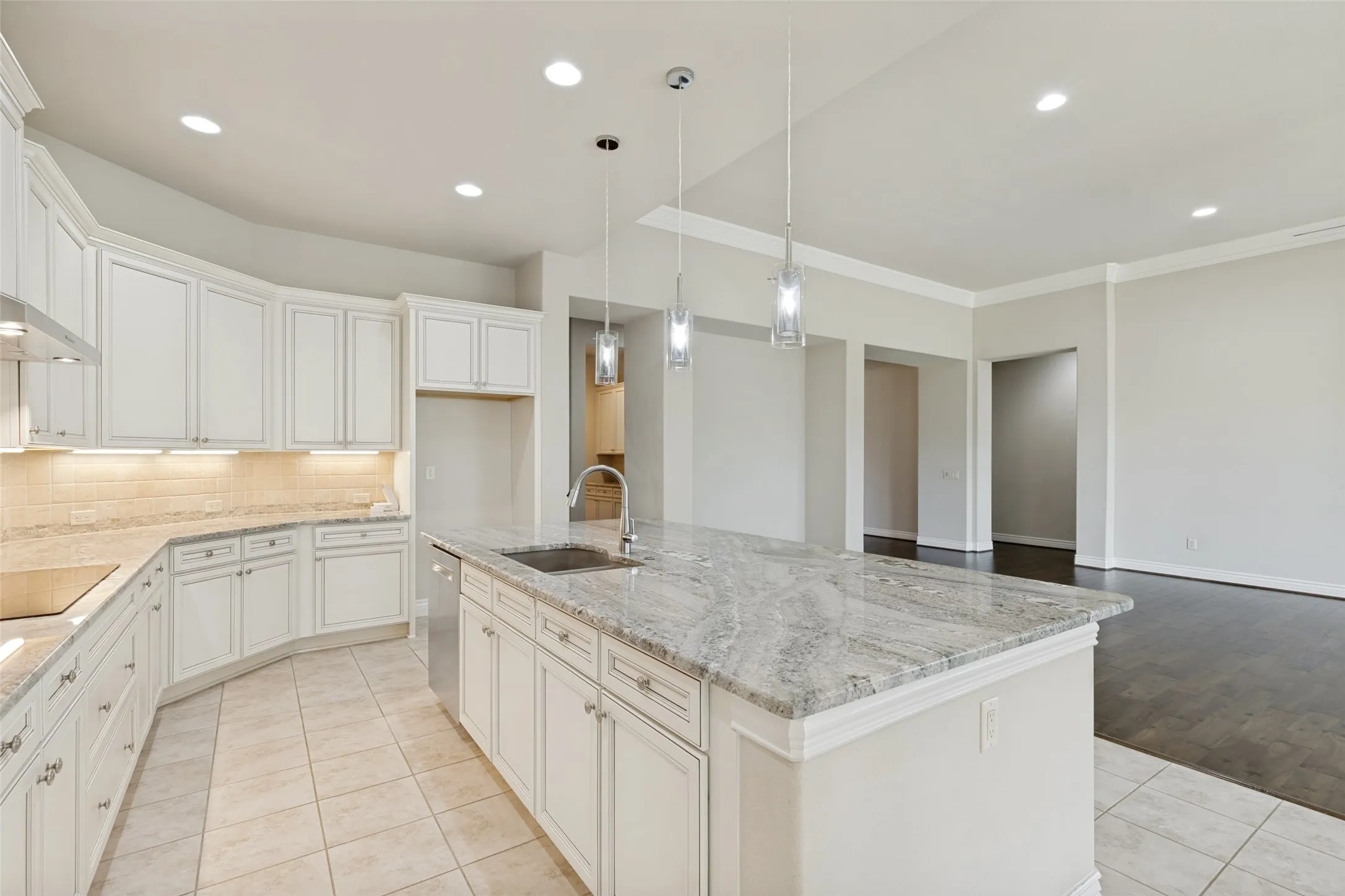 Expansive kitchen featuring a large island with a stone countertop, white cabinetry with undermount lighting, and tile flooring