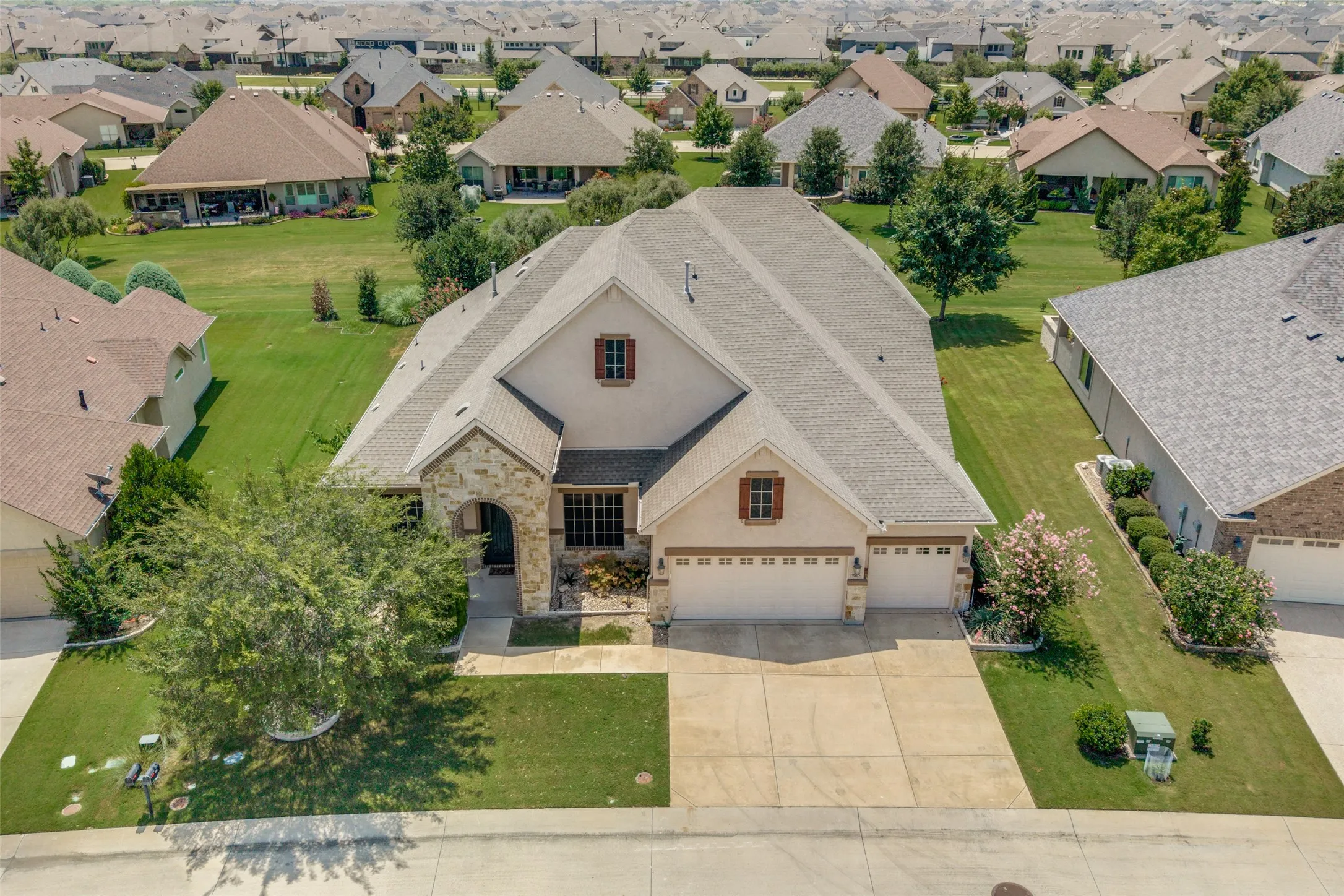 Stucco and stone facade home featuring a multi-car driveway, arched entry, and a gabled roof