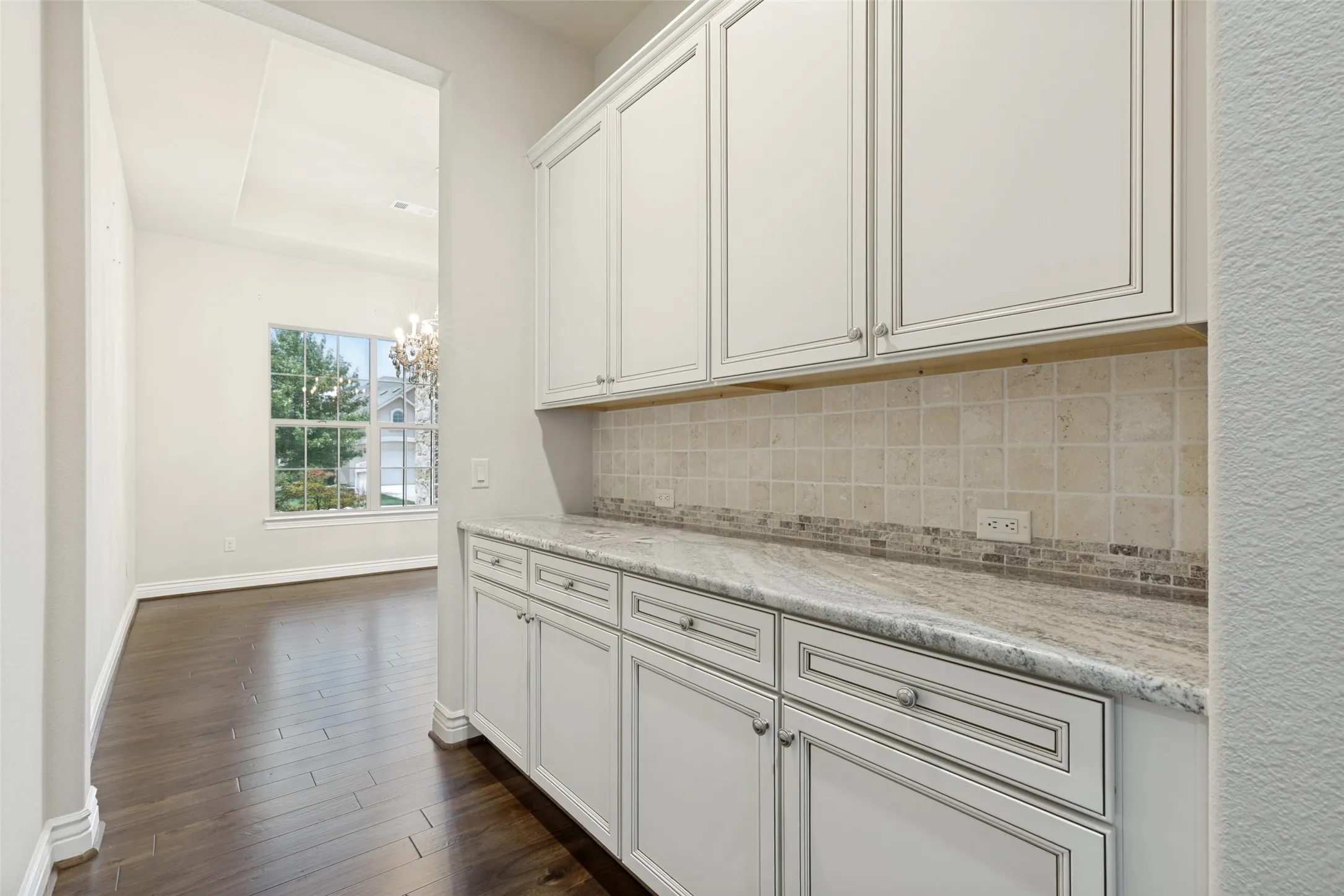 Built-in white cabinetry with decorative trim, light-toned countertop, and tiled backsplash