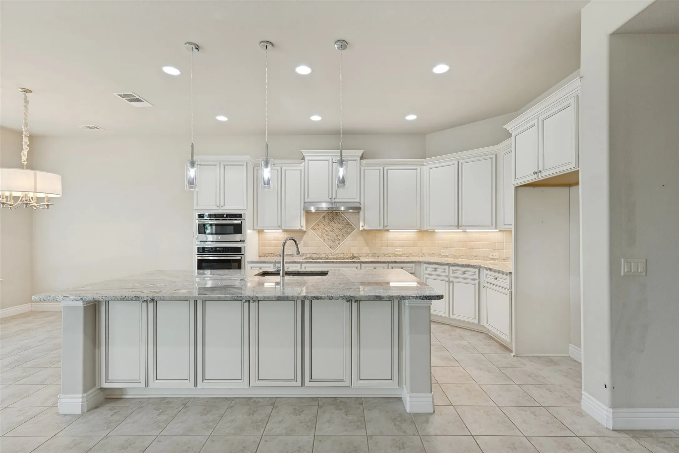 Expansive kitchen featuring a large island with a stone-finish countertop, white cabinetry, built-in double ovens, and recessed lighting