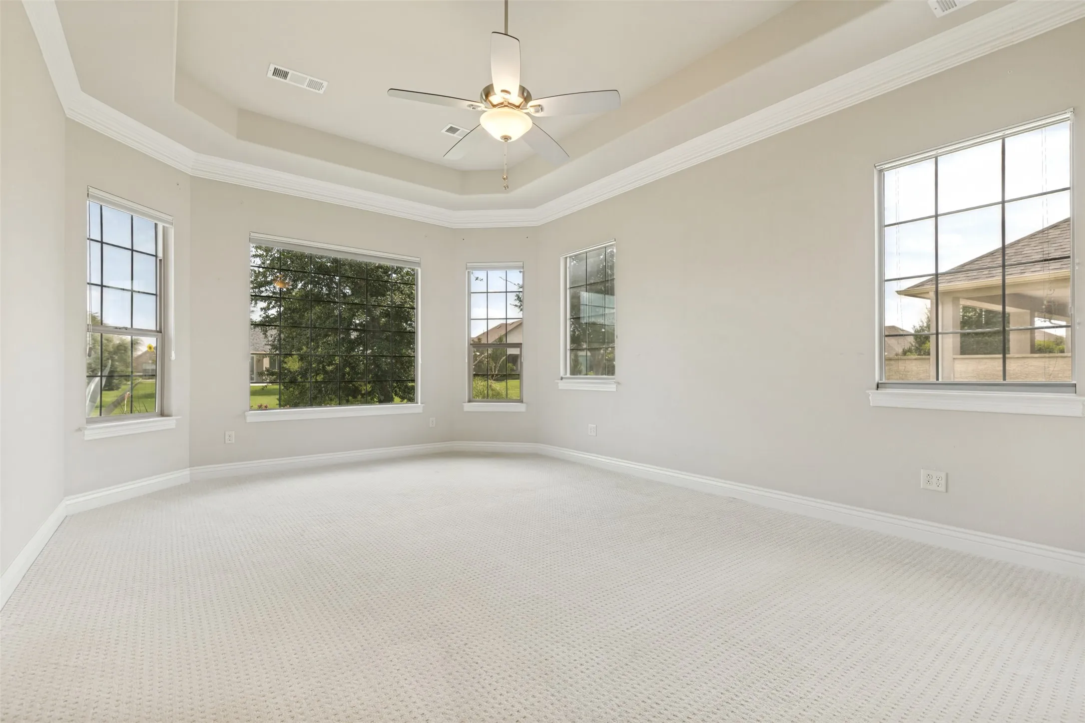 Spacious room featuring light-colored carpet flooring, a tray ceiling, and a ceiling fan