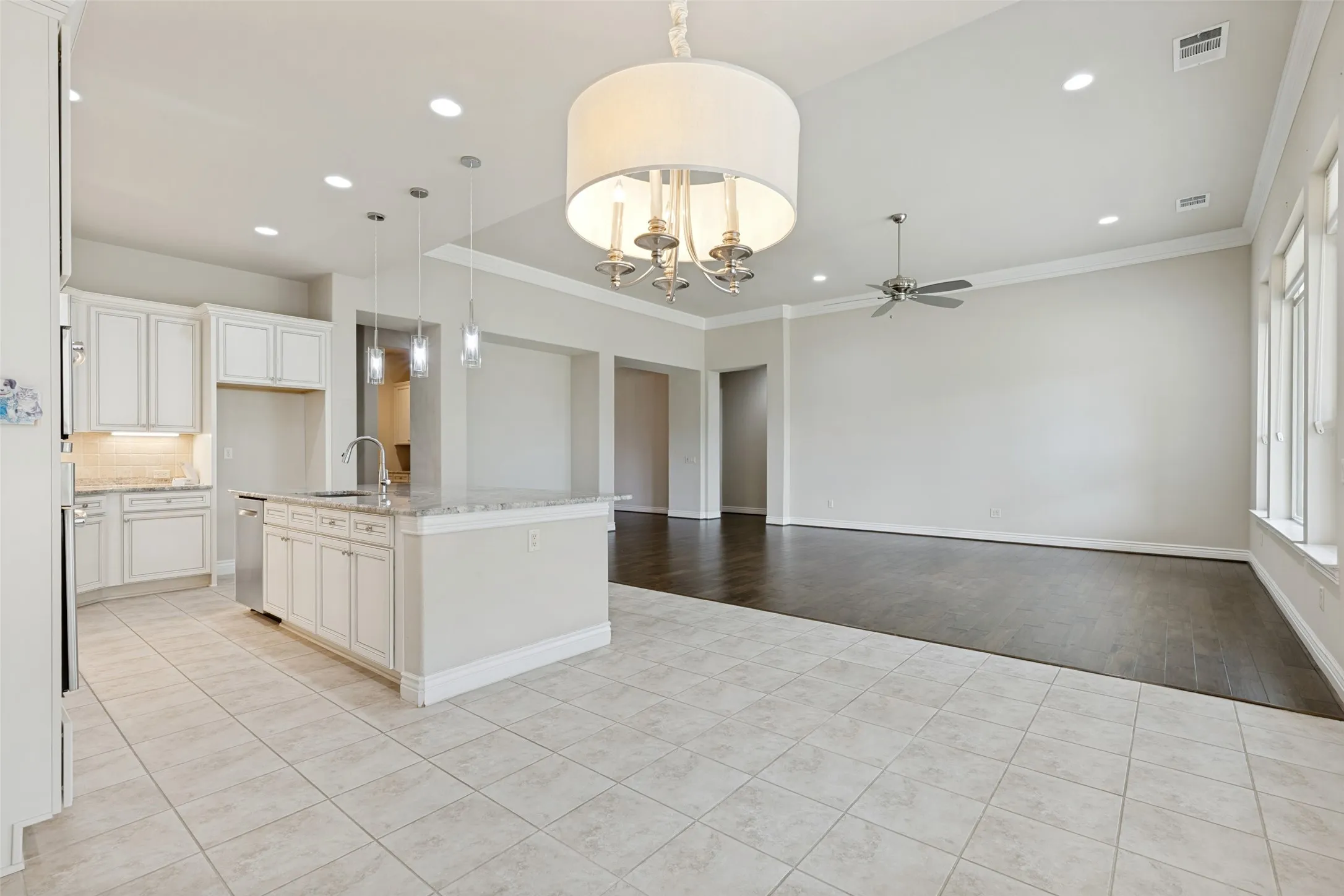 Open-concept living area featuring a kitchen island with pendant lighting, white cabinetry, integrated stainless steel appliances, and tile flooring