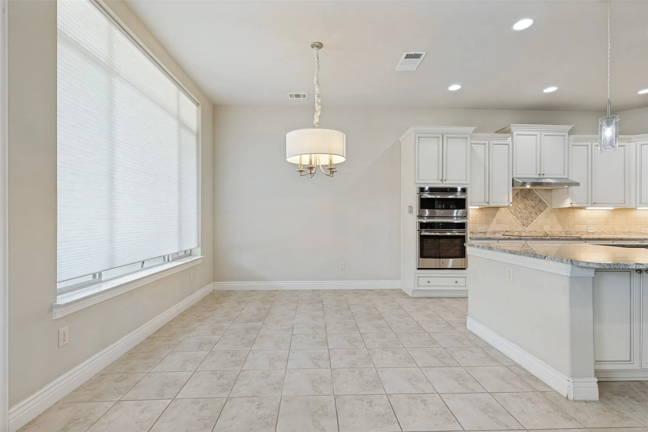 Bright dining area featuring tile flooring, a large window with blinds, and a drum pendant light fixture