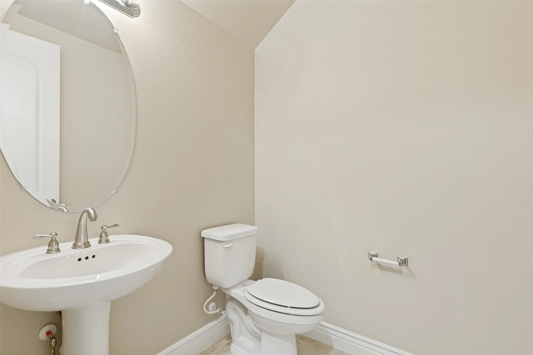 Pedestal sink with a polished nickel faucet, oval framed mirror, and warm neutral wall color