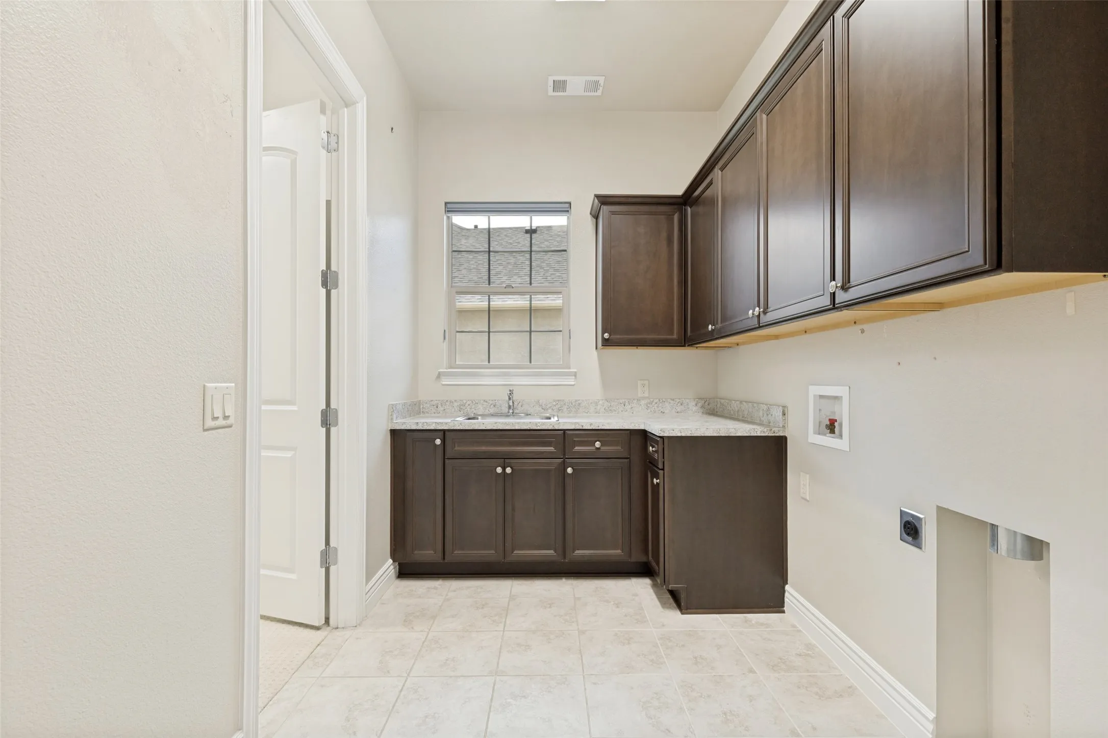Utility room featuring dark wood-finish cabinetry, a sink with a chrome faucet, light-toned countertop, and tiled flooring