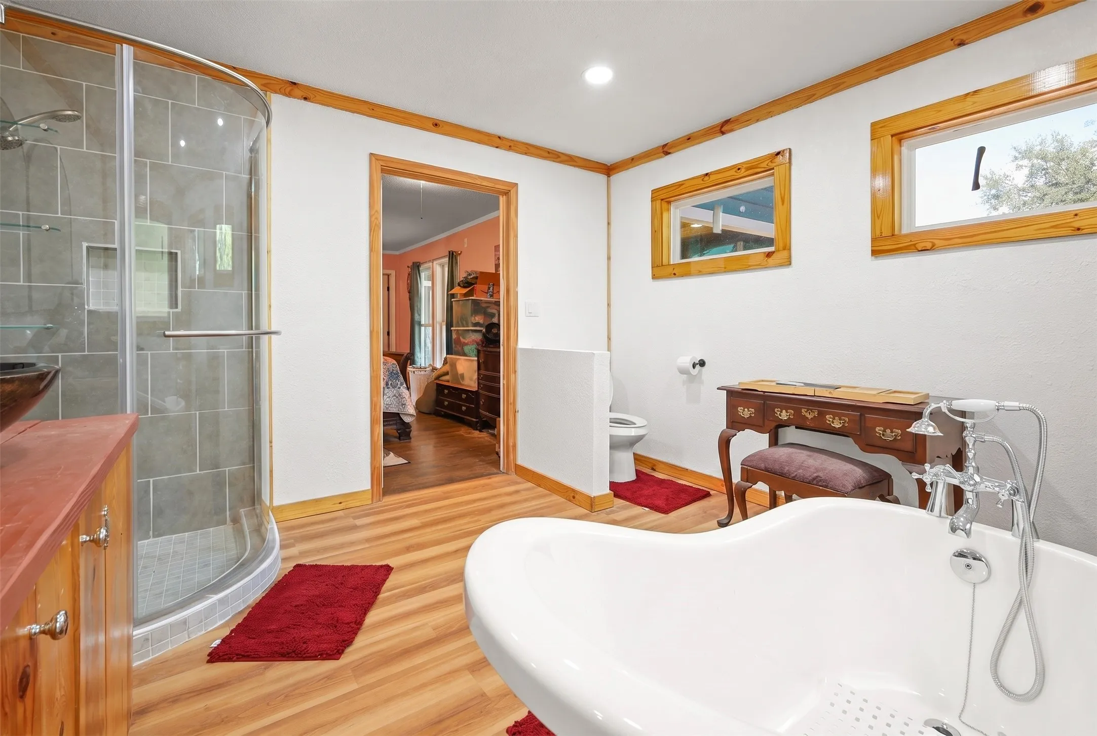 Bathroom featuring a freestanding soaking tub, wood-finish flooring, a curved glass shower enclosure with gray tile, and wood-framed windows