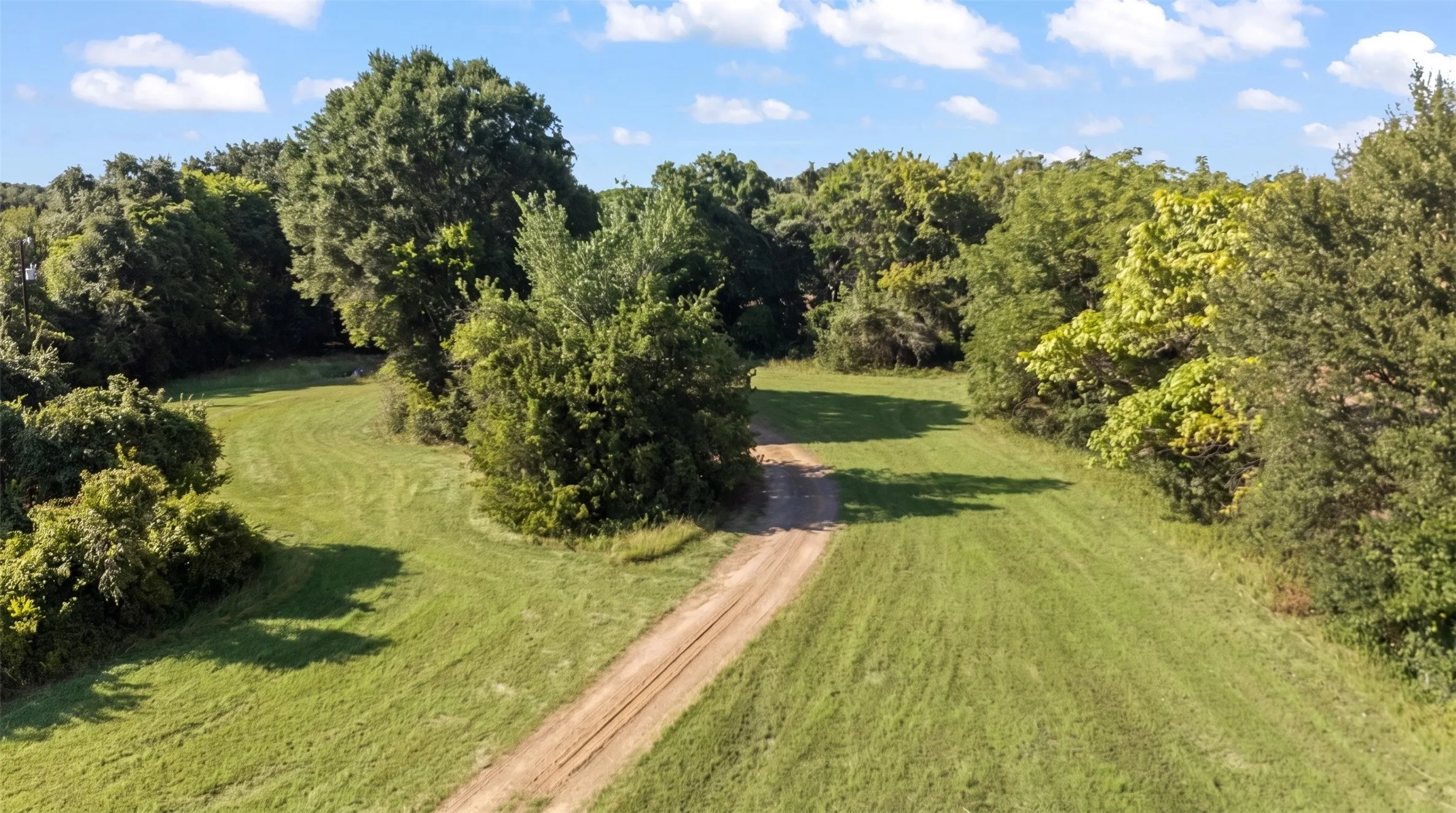 Expansive cleared land featuring a dirt track, surrounded by mature trees and natural foliage