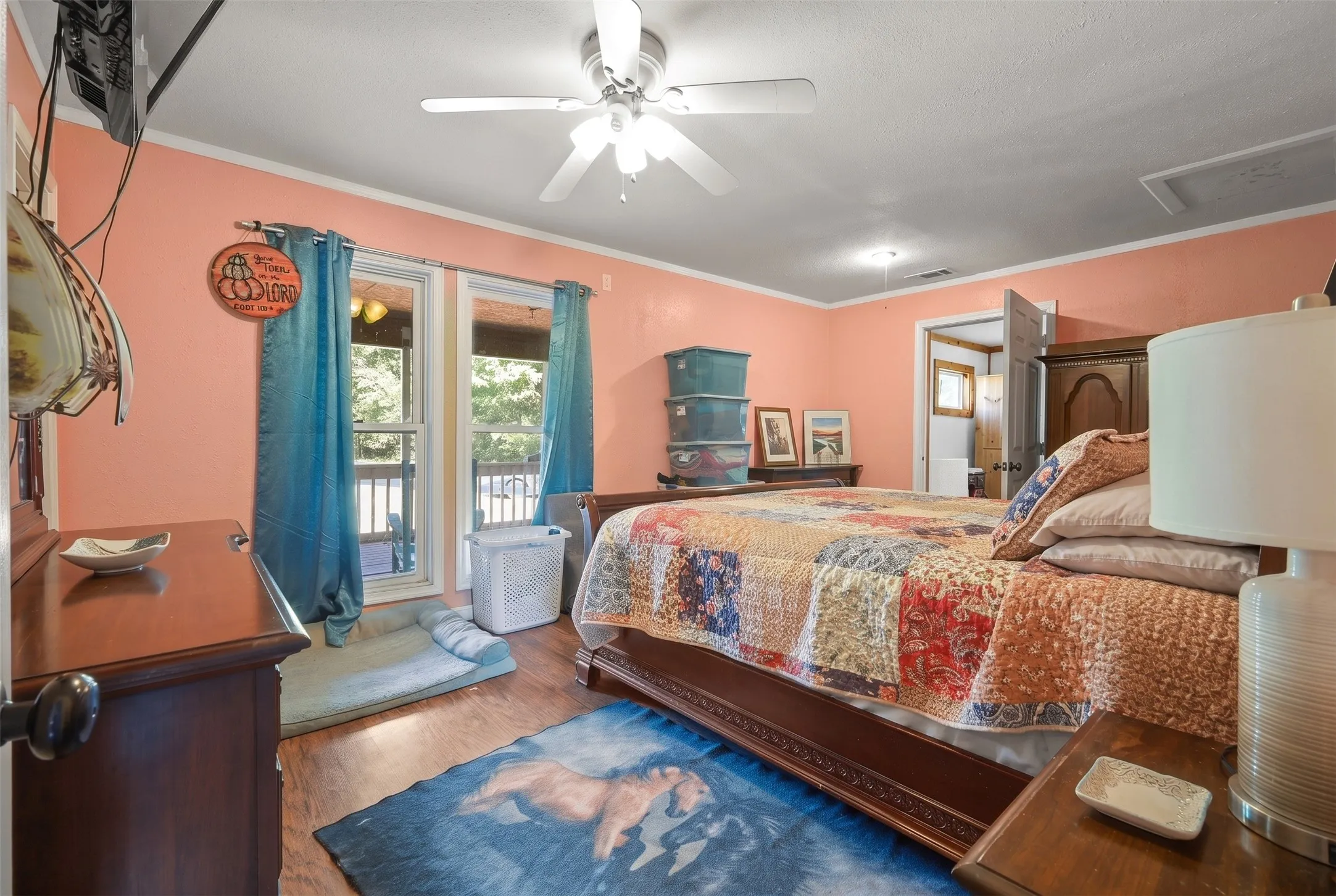 Spacious room with wood-finish flooring, featuring a ceiling fan, crown molding, and direct outdoor access through twin windows