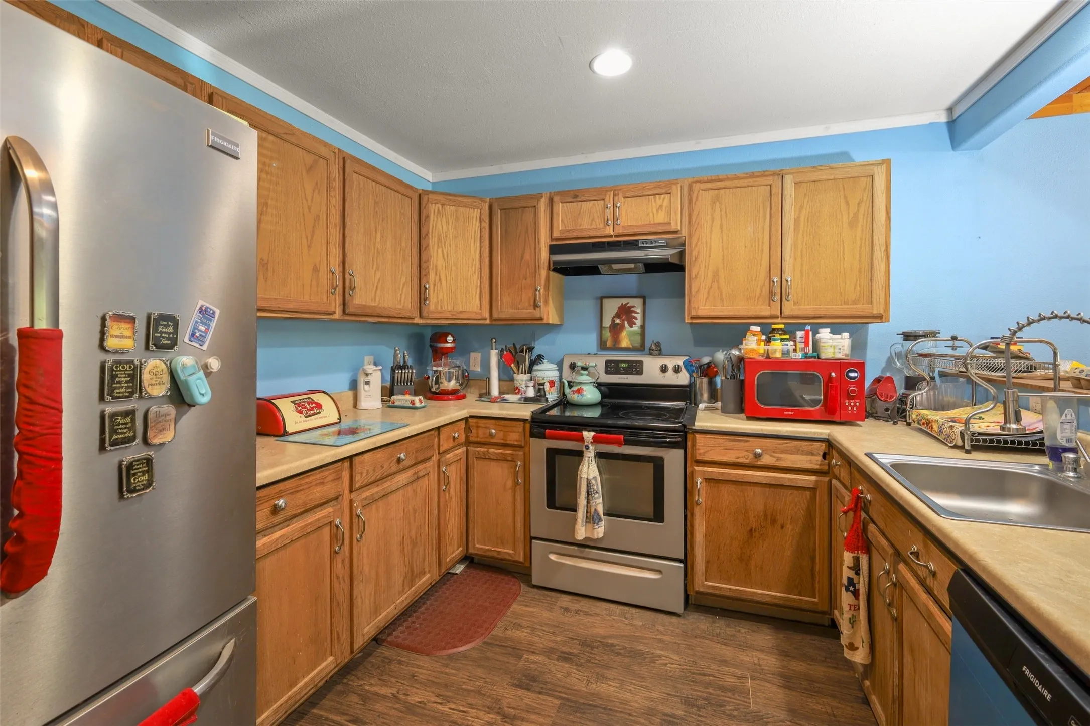 Wood-finish flooring complementing light wood cabinetry, stainless steel appliances, and a built-in kitchen sink