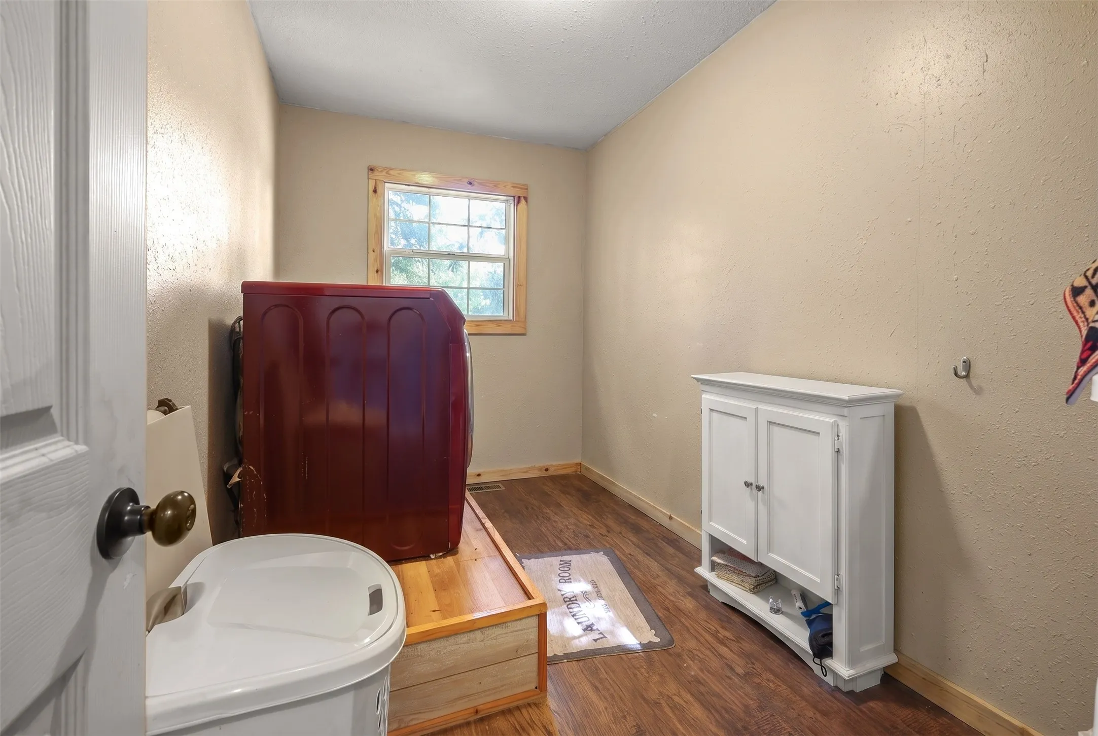 Utility room featuring wood-finish flooring, a window with wood trim, and neutral-toned walls