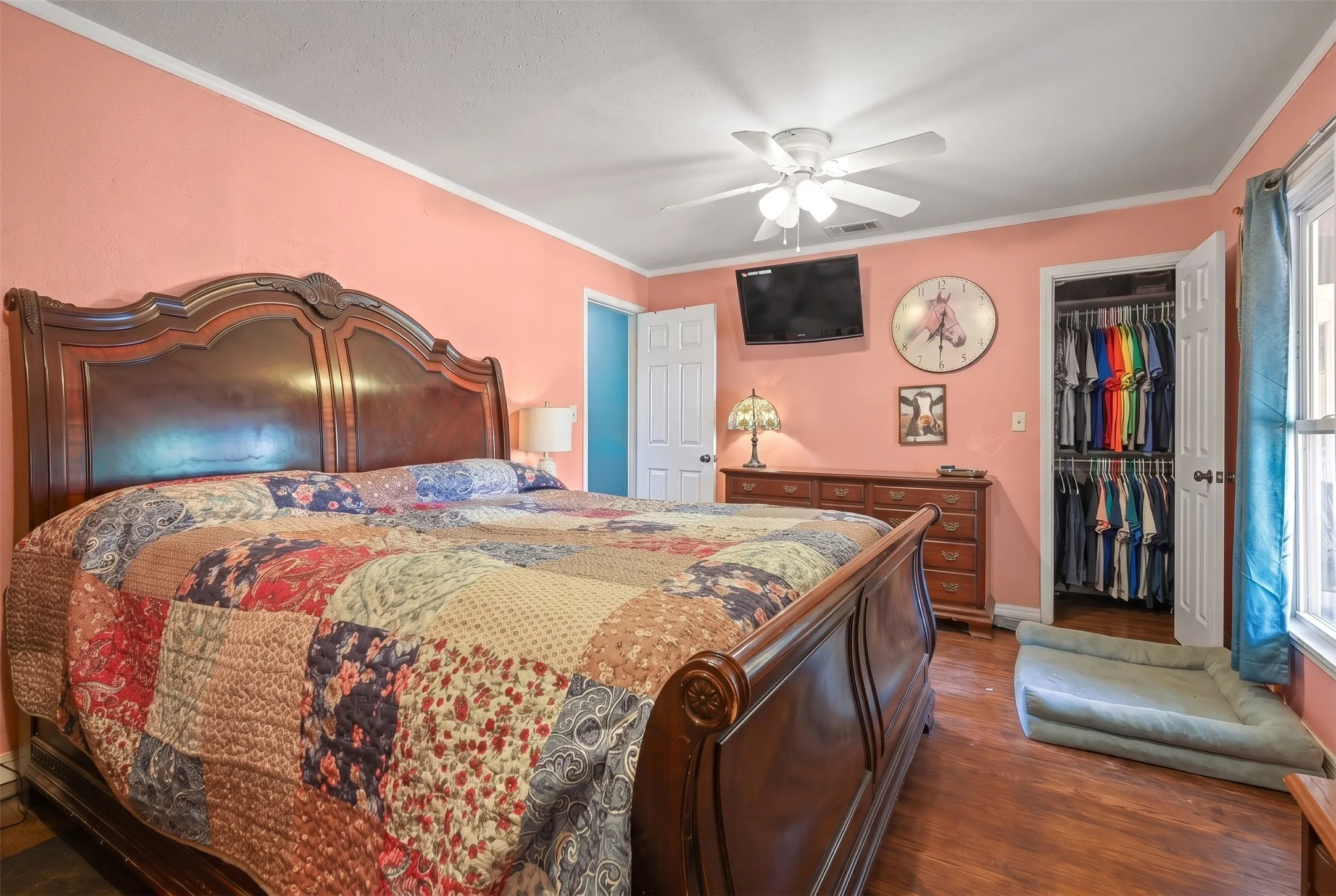 Spacious room featuring wood-finish flooring, a ceiling fan with integrated lighting, and a closet with a bifold door and built-in shelving
