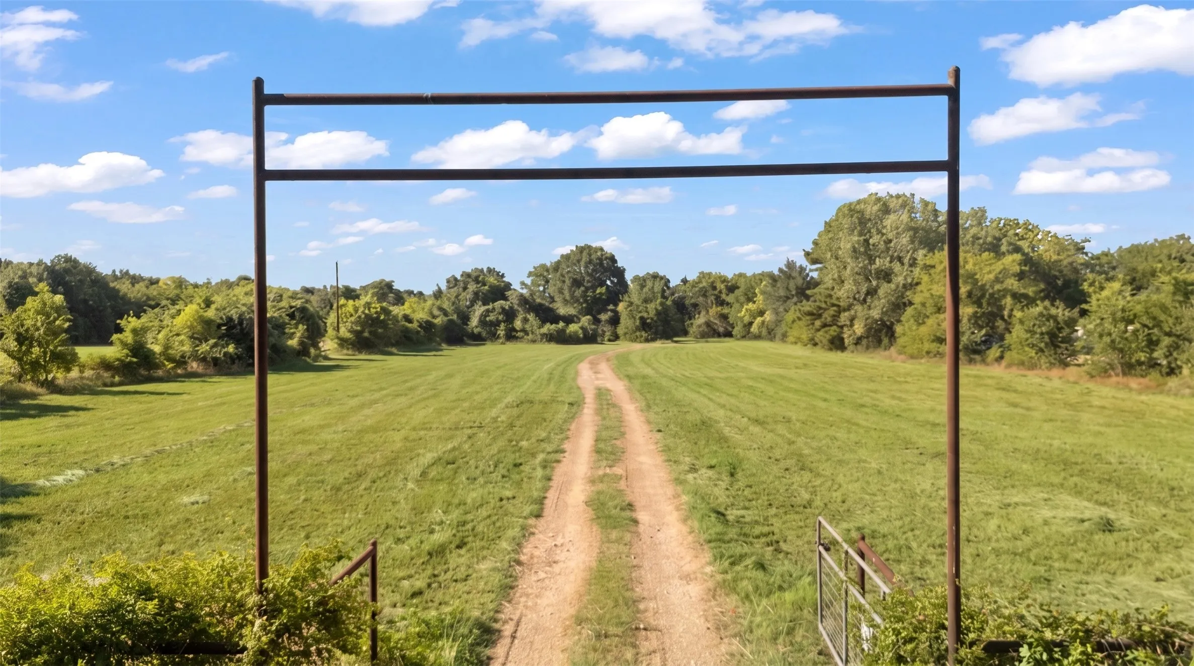 Expansive rural property featuring a prominent metal entry arch and a dirt drive