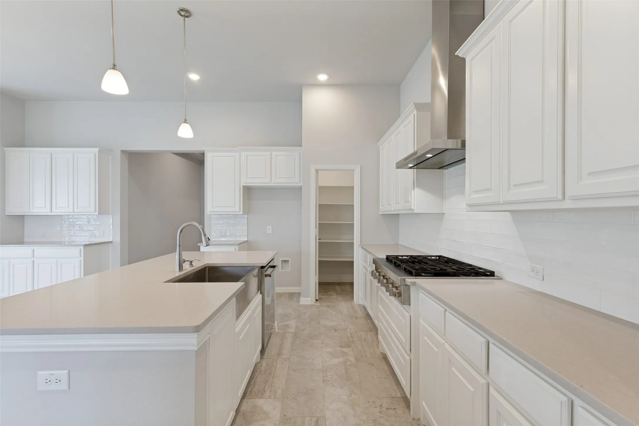 Spacious kitchen featuring white cabinetry, light-toned countertops, a professional-style 6-burner gas cooktop, a sleek modern vent hood, and a classic white subway tile backsplash