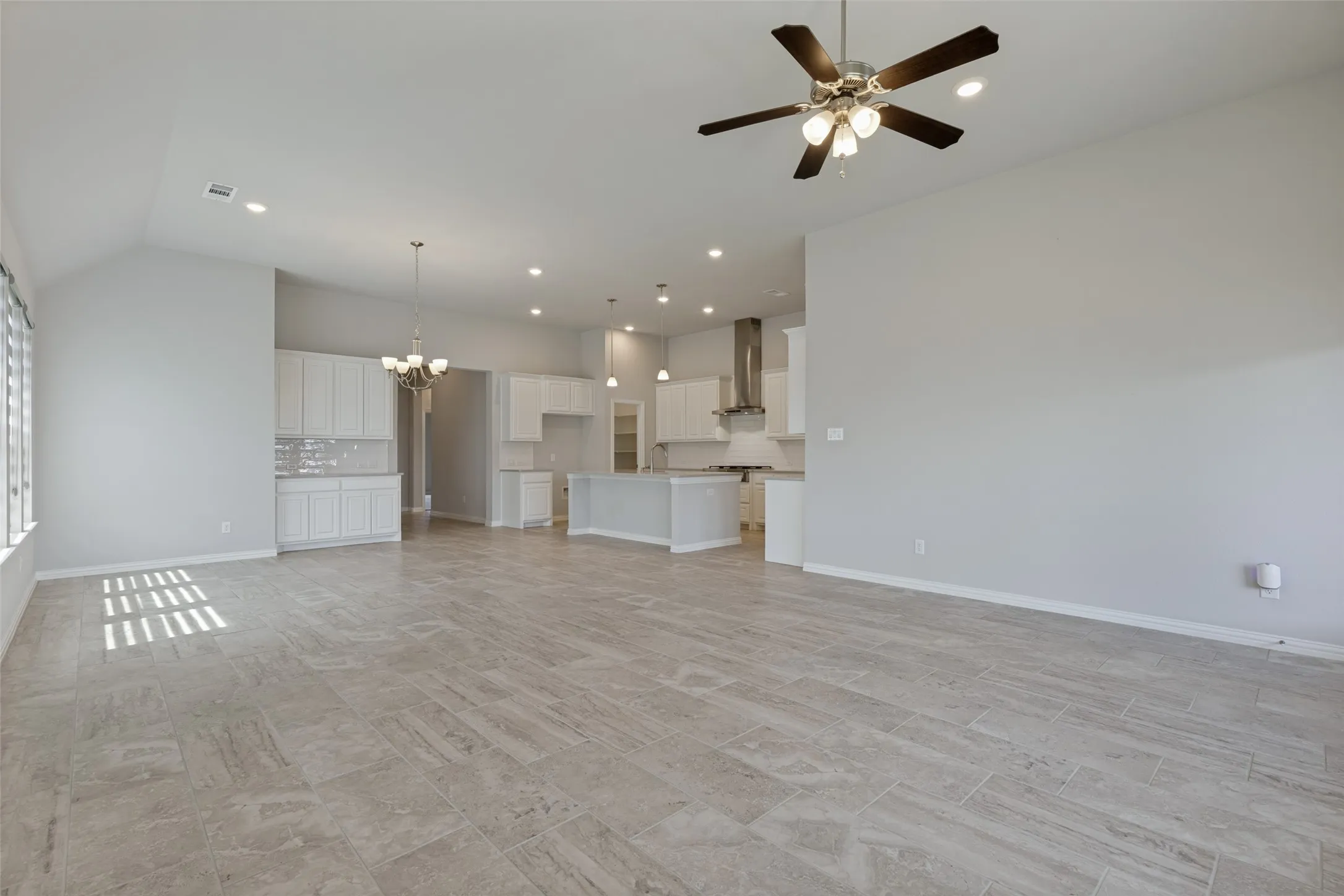 Spacious open-concept interior featuring light gray tile flooring, vaulted ceilings, and recessed lighting