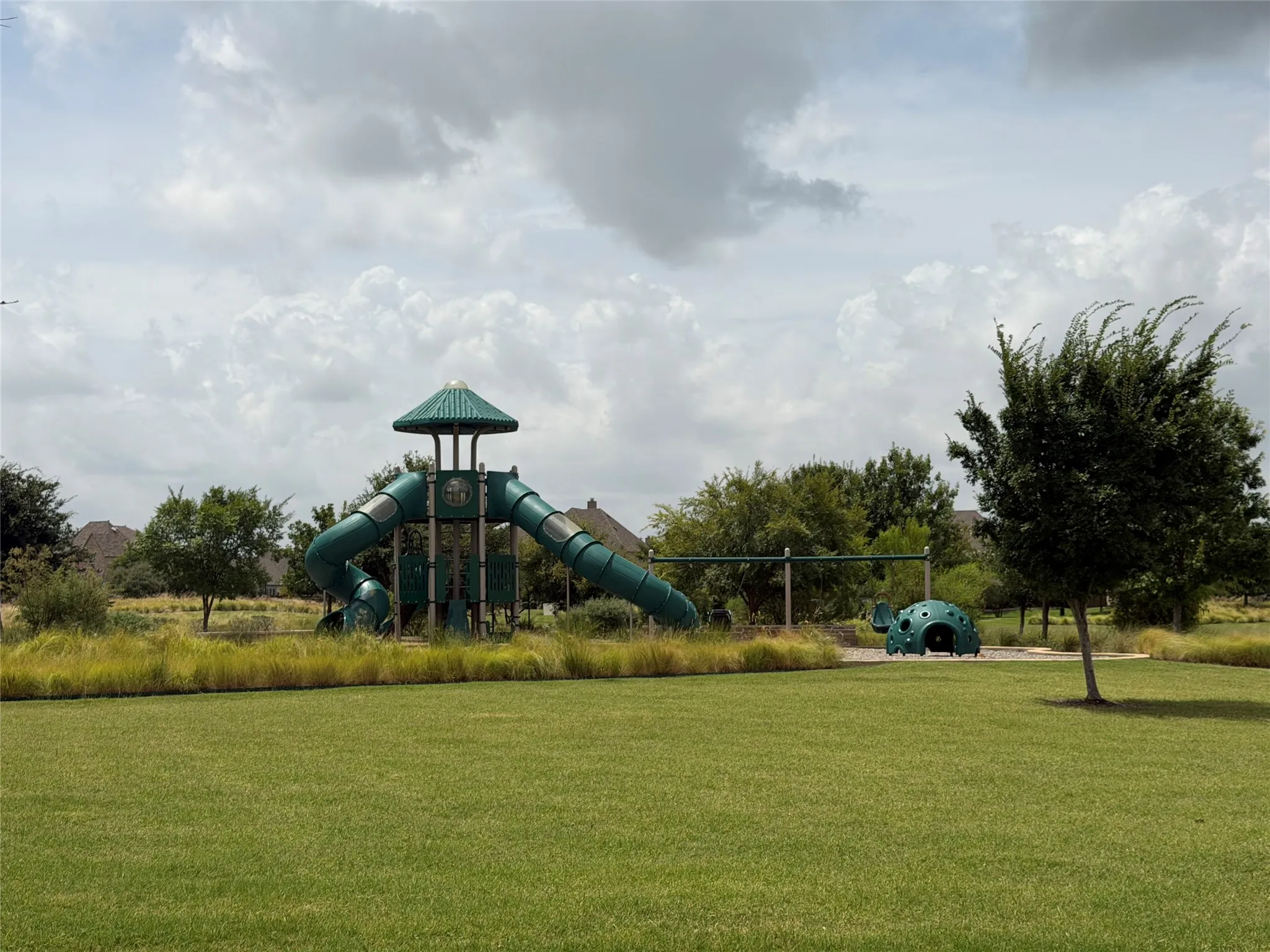 Expansive green space featuring a playground with a tower, multiple slides, and a swingset