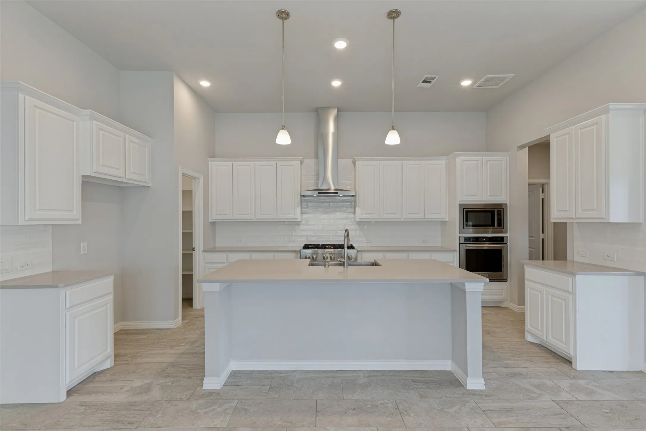 Modern kitchen featuring white shaker cabinetry, light-toned countertops, a central island with a sink, stainless steel appliances, and recessed lighting