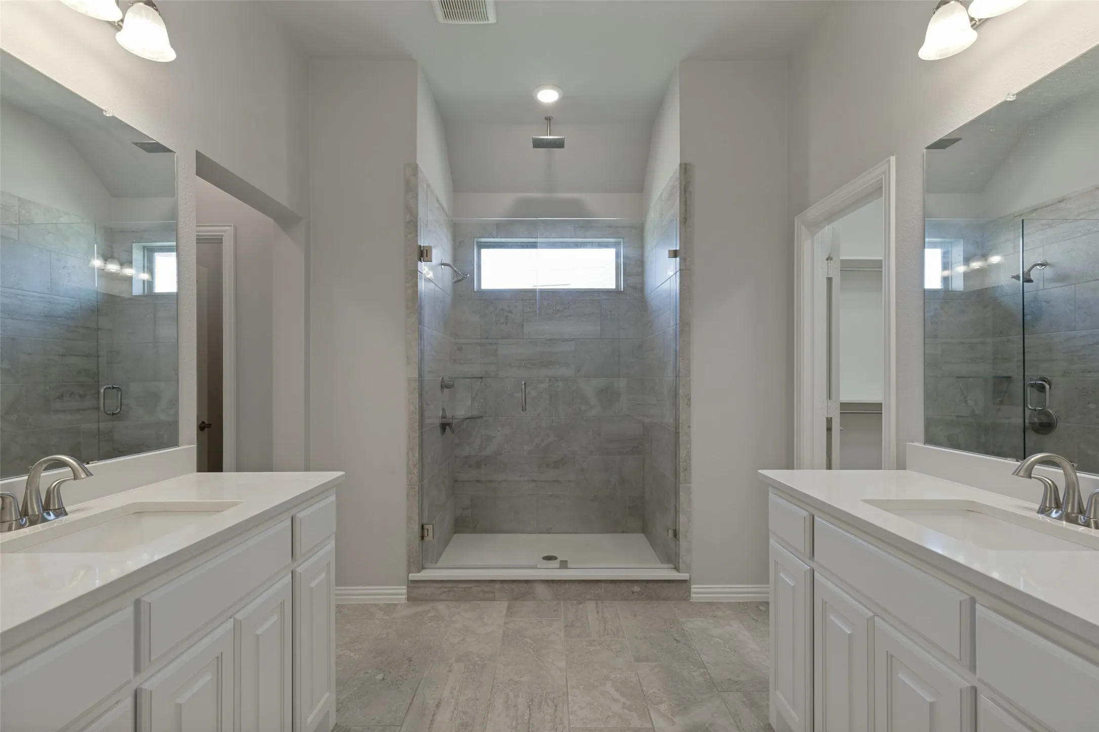 Spacious bathroom featuring a large walk-in shower with full-height tile surround, dual vanity sinks with white cabinetry, light-toned countertops, and brushed nickel fixtures