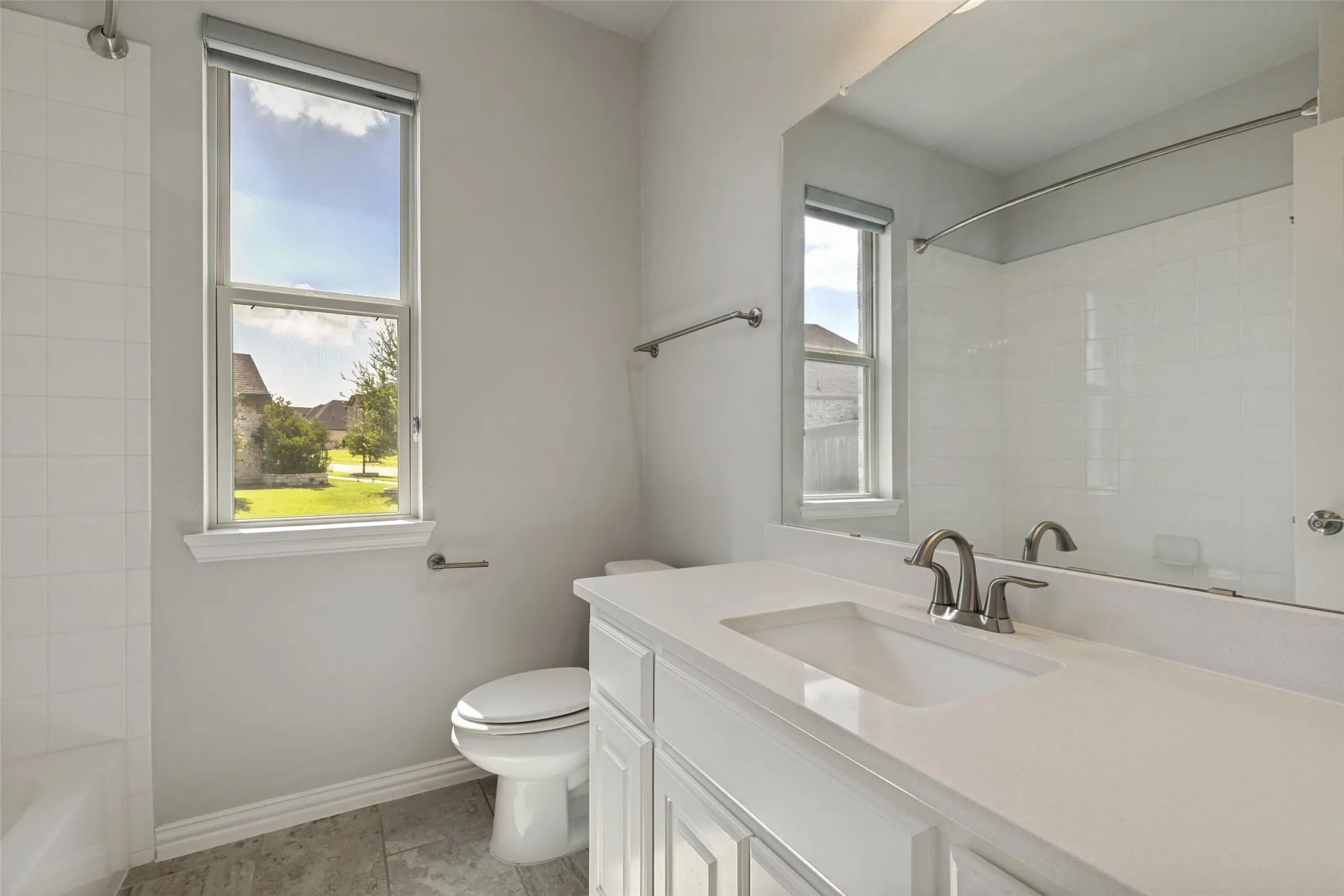 Bathroom featuring a white vanity with an integrated sink and brushed nickel faucet, a large rectangular mirror, and a window with a roller shade