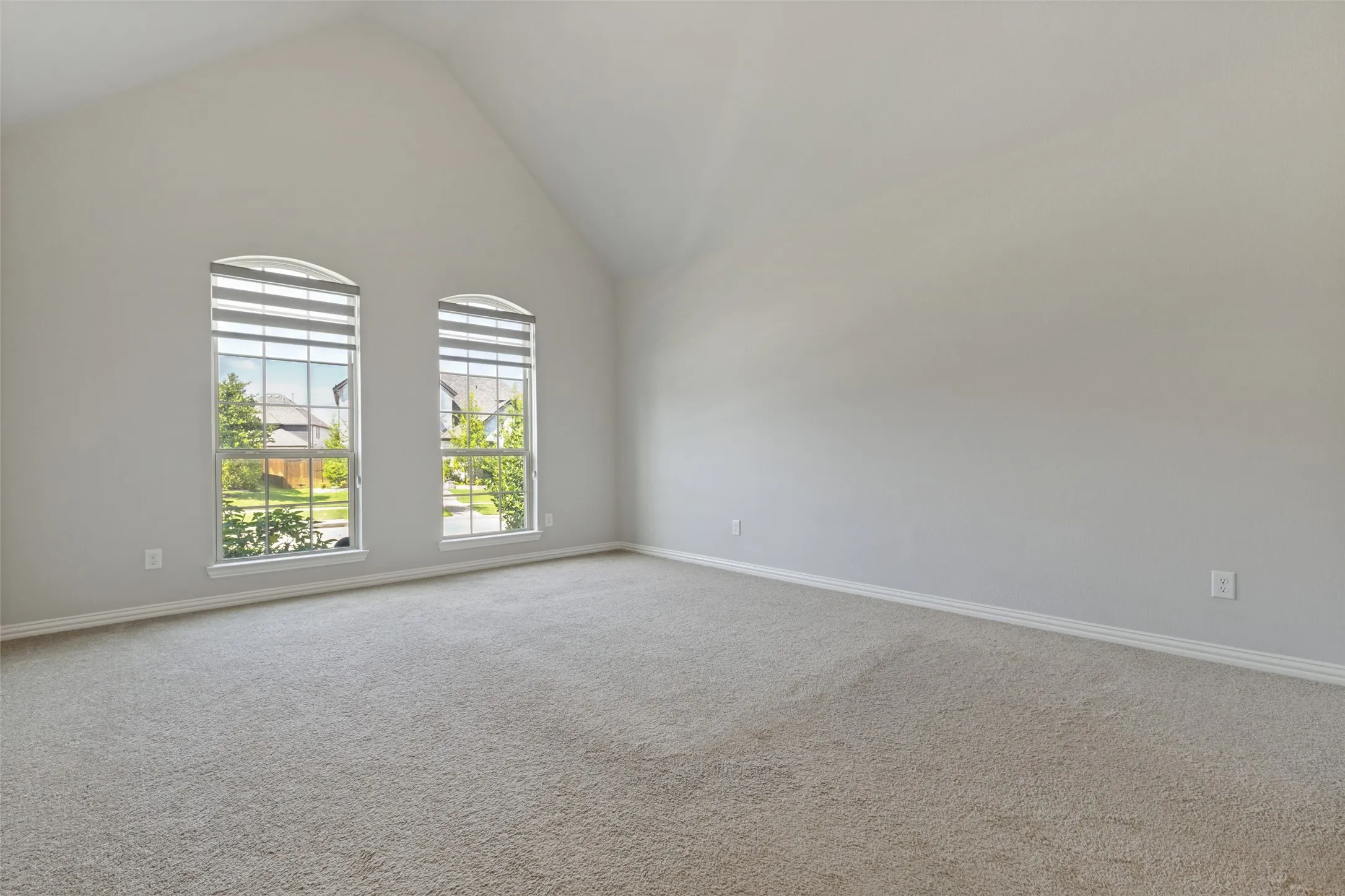 Vaulted ceiling room featuring twin arched windows with louvered blinds, carpeting, and neutral wall tones