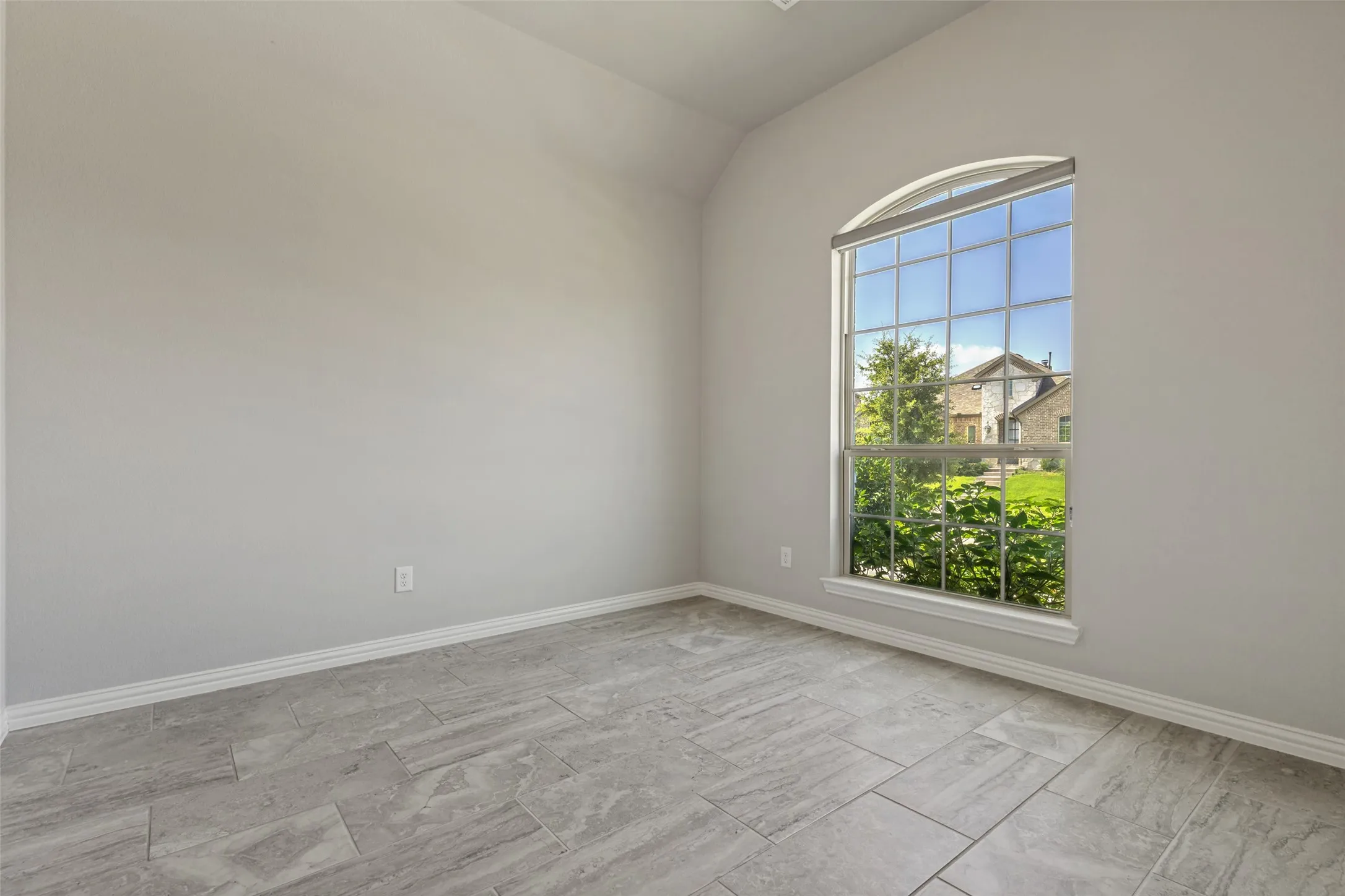 Arched window offering natural light, complemented by light gray paint and a vaulted ceiling