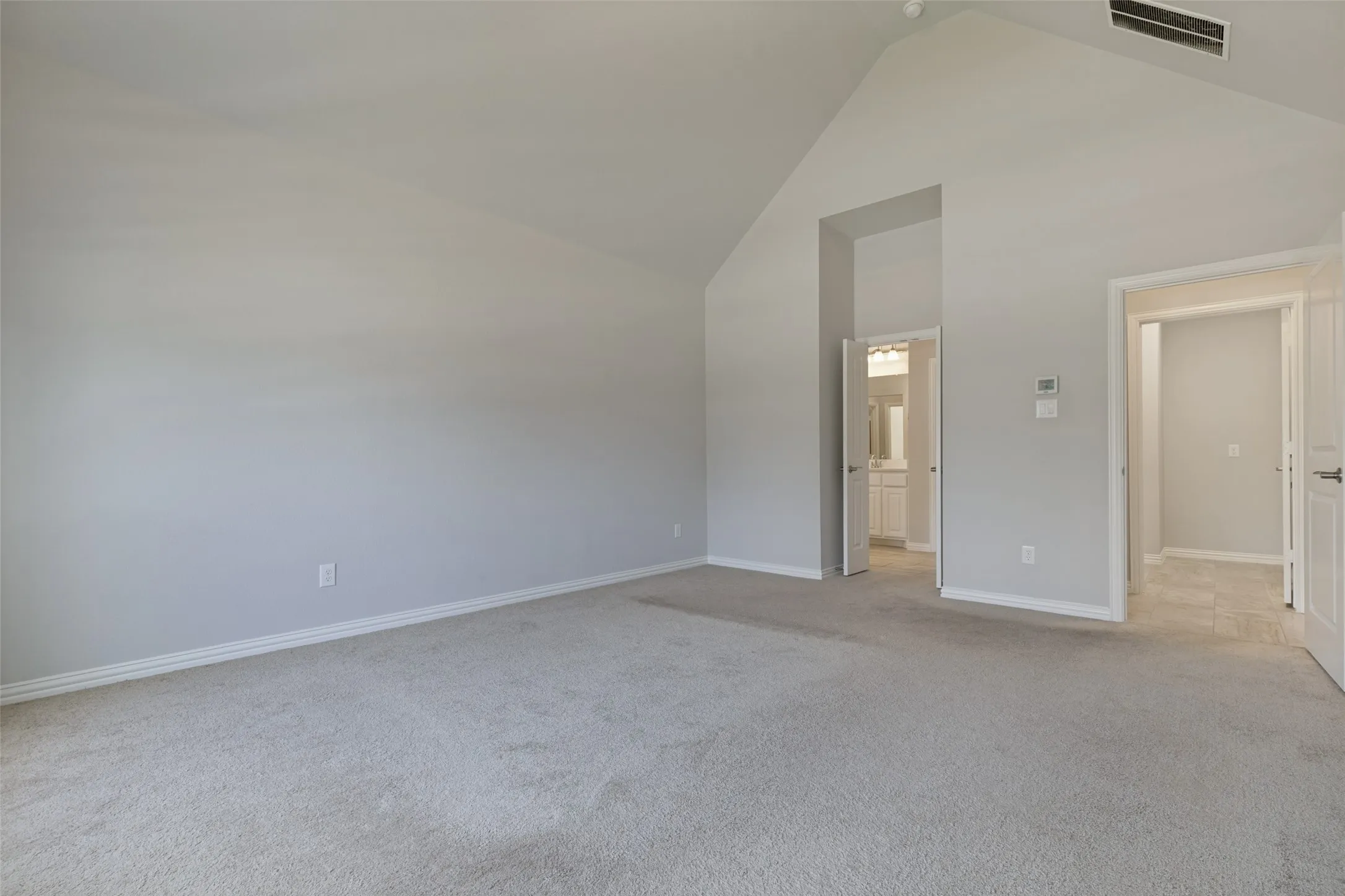 Spacious interior room featuring a vaulted ceiling, light gray wall paint, and carpeting