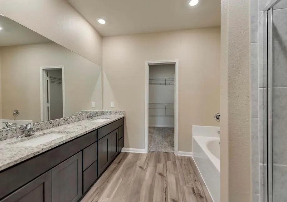 Spacious bathroom featuring a dual vanity with light-toned countertops, wood-finish flooring, a built-in tub, and a separate shower enclosure