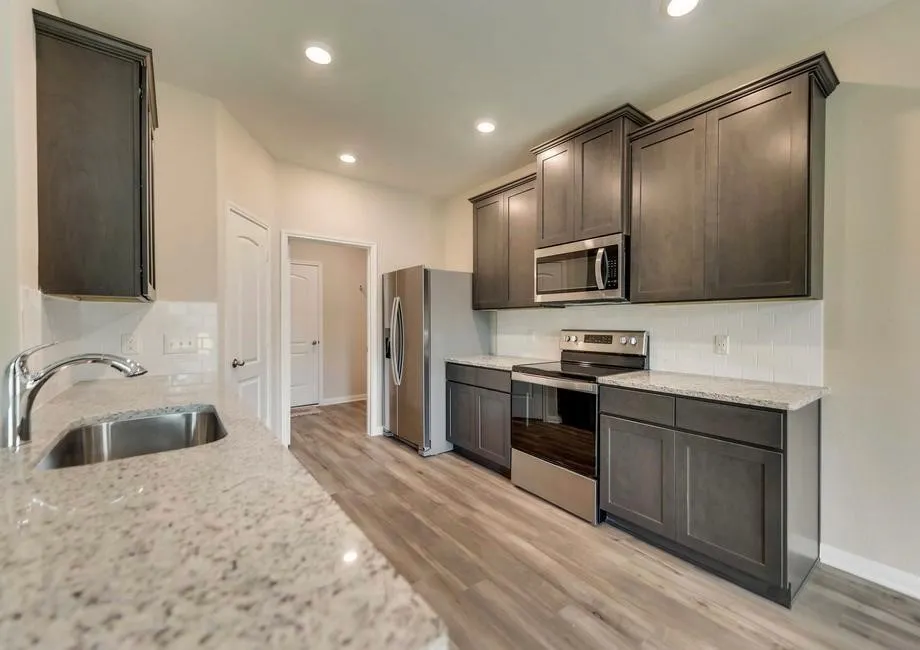 Contemporary kitchen featuring dark wood-finish cabinetry, light speckled countertops, stainless steel appliances, a subway tile backsplash, and recessed lighting