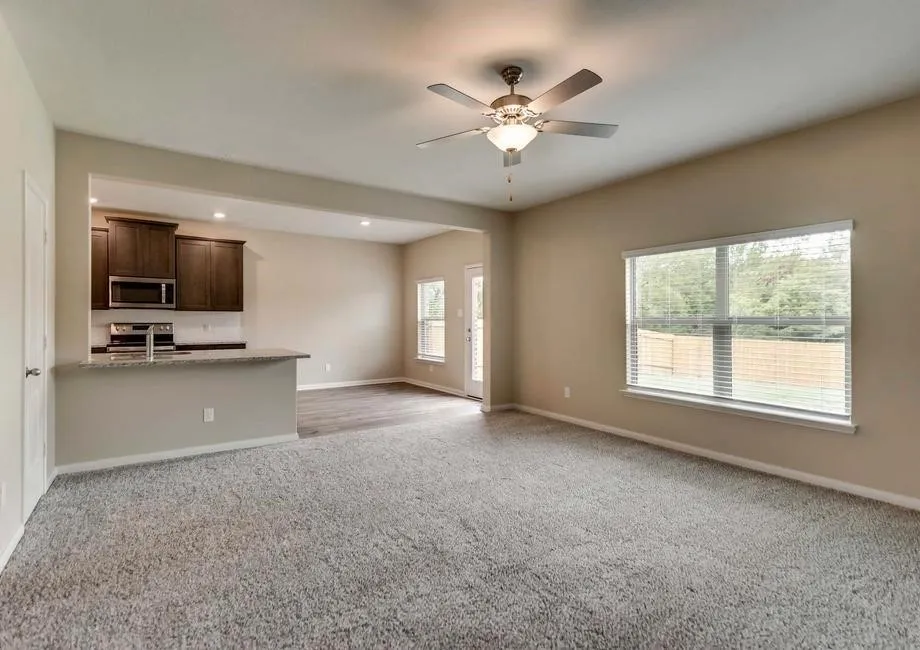 Spacious living area featuring carpet flooring, a ceiling fan with integrated lighting, and large windows with blinds