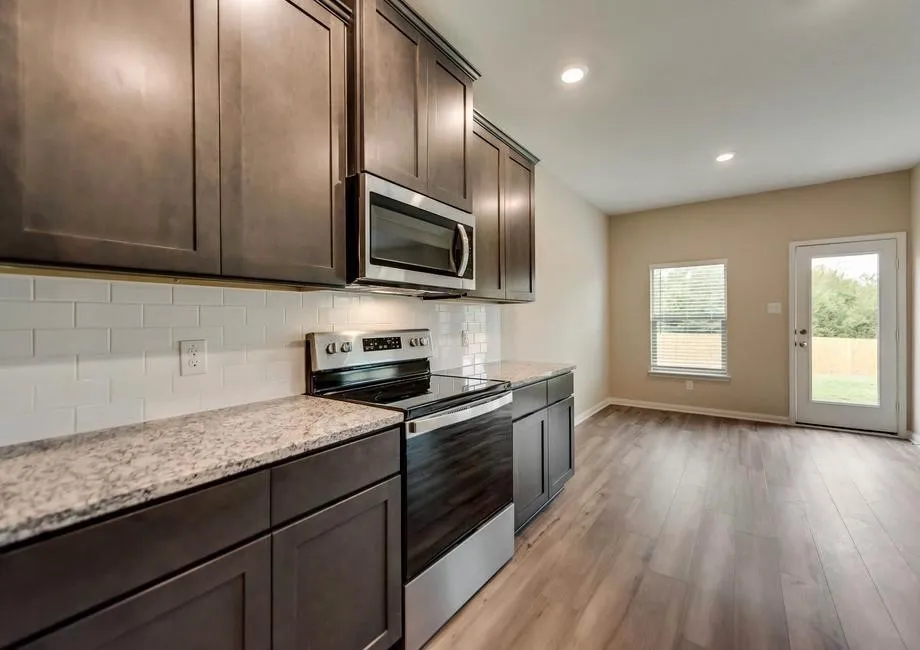 Kitchen featuring dark wood cabinetry, light-toned countertops, white subway tile backsplash, and stainless steel appliances