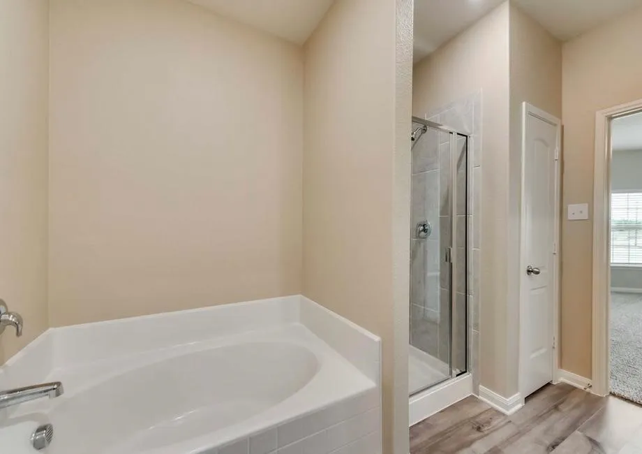 Corner soaking tub with chrome fixtures, glass-enclosed shower with tiled surround, and wood-finish flooring