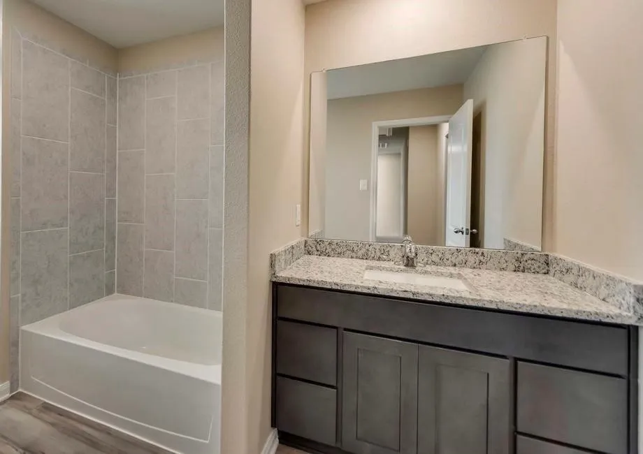 Bathroom featuring a gray wood-finish vanity with a light speckled countertop, an integrated sink, and a large wall-mounted mirror