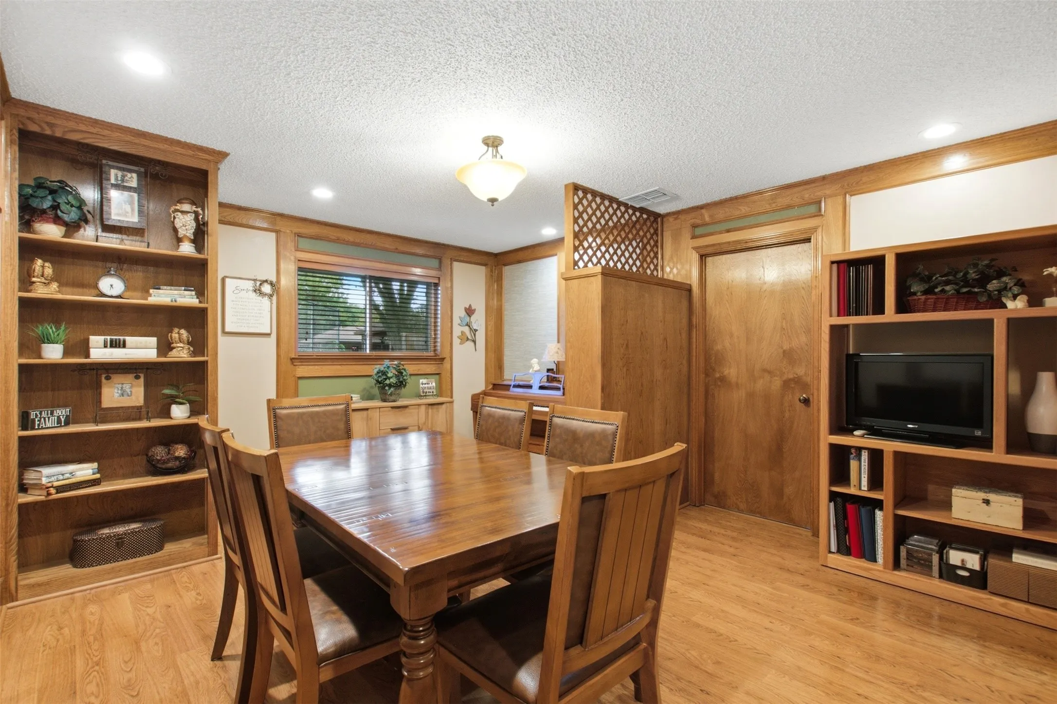 Dining area featuring wood-finish flooring, built-in shelving, wood trim accents, a window with blinds, and recessed lighting