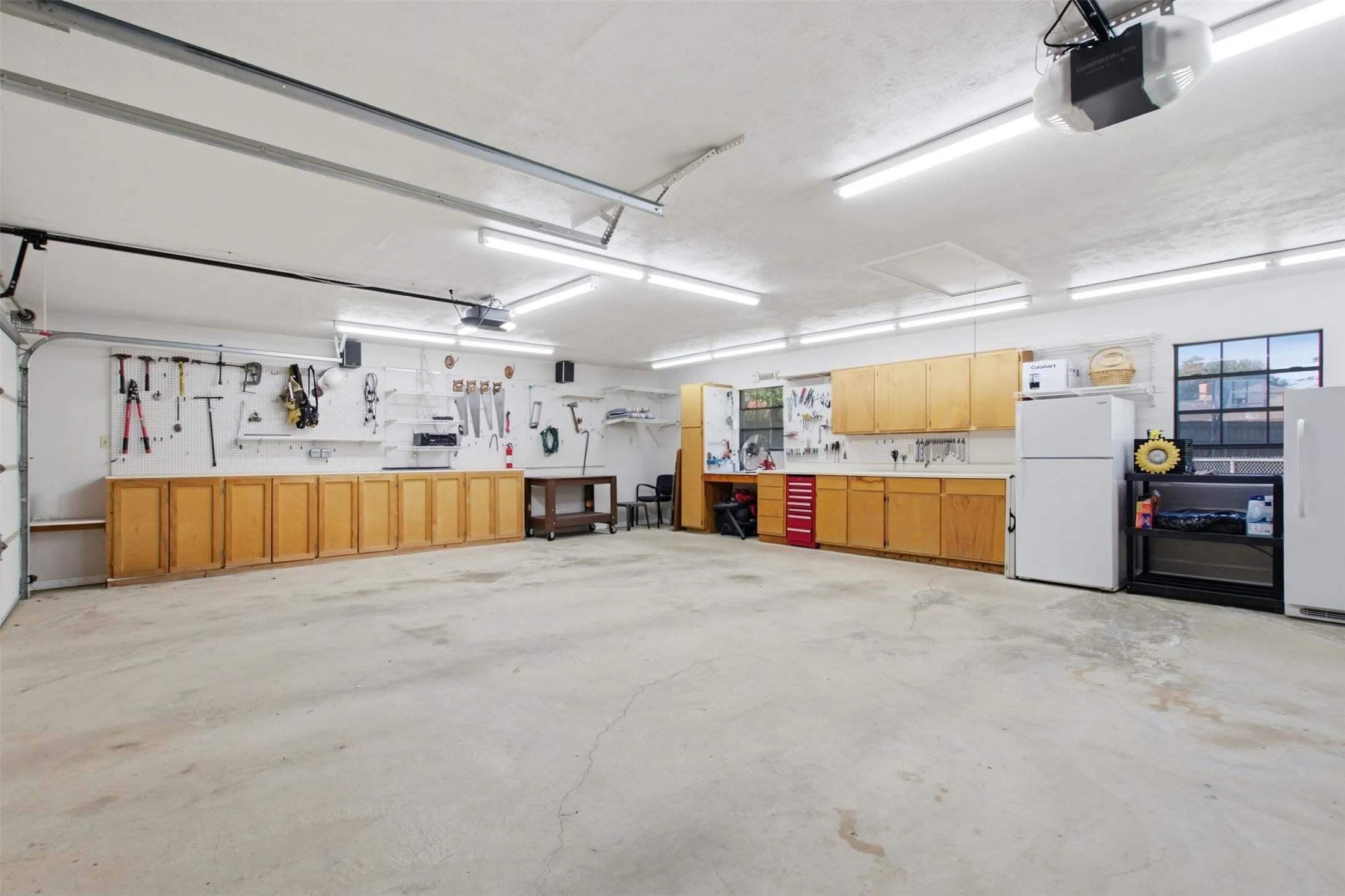 Spacious garage featuring extensive built-in cabinetry, durable concrete flooring, ample overhead lighting, and two windows providing natural light