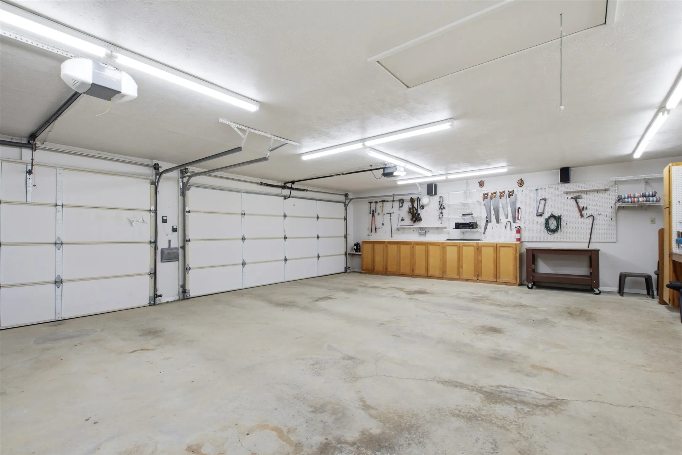 Spacious two-car garage featuring automatic openers, extensive overhead fluorescent lighting, and built-in wood cabinetry for organized storage