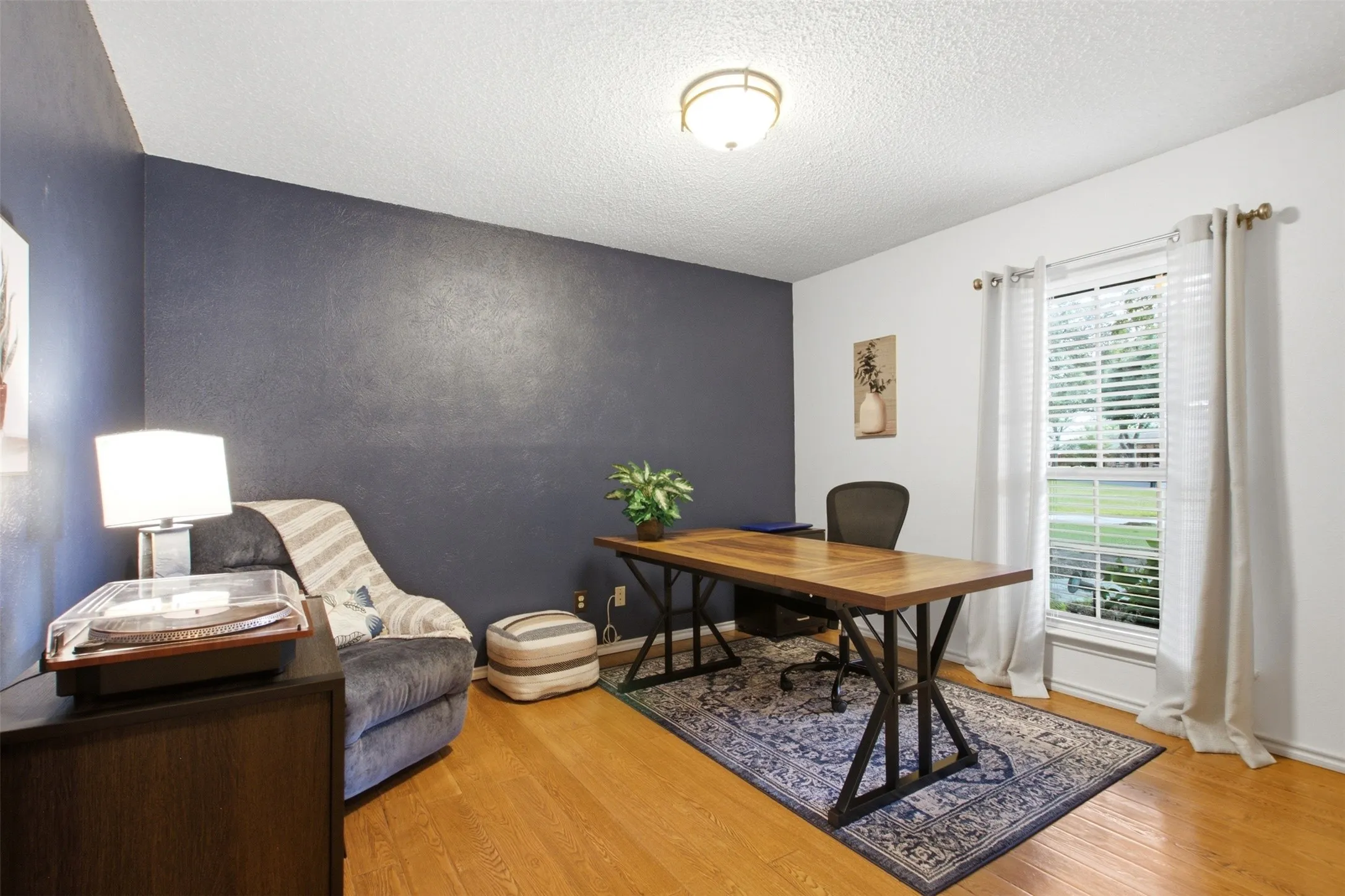 Bedroom used as office featuring wood-finish flooring, a painted accent wall, and a window with blinds