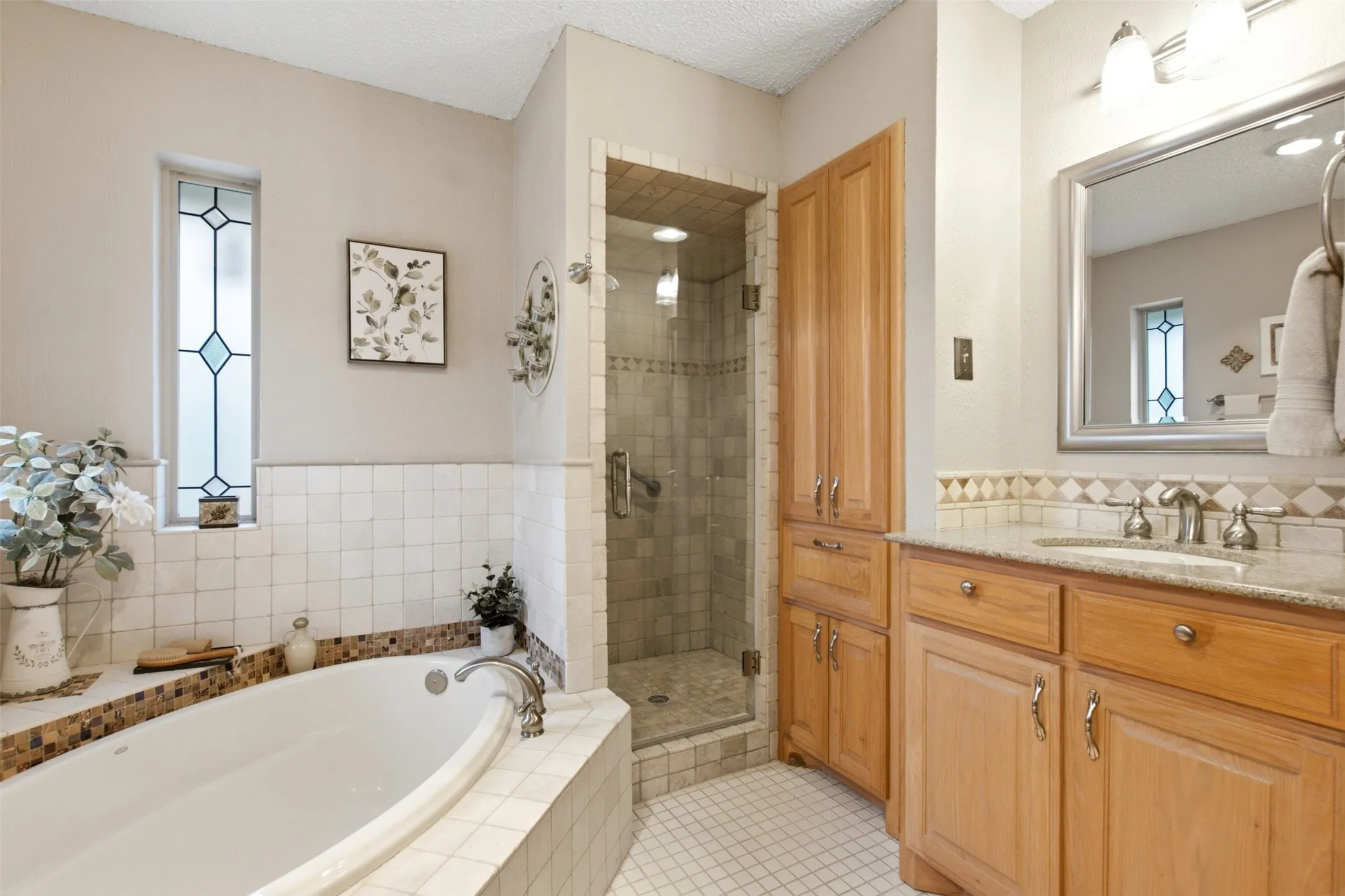 Spacious bathroom featuring a built-in soaking tub, a tiled walk-in shower with a glass enclosure, and a vanity with natural wood-finish cabinetry and a light-toned countertop