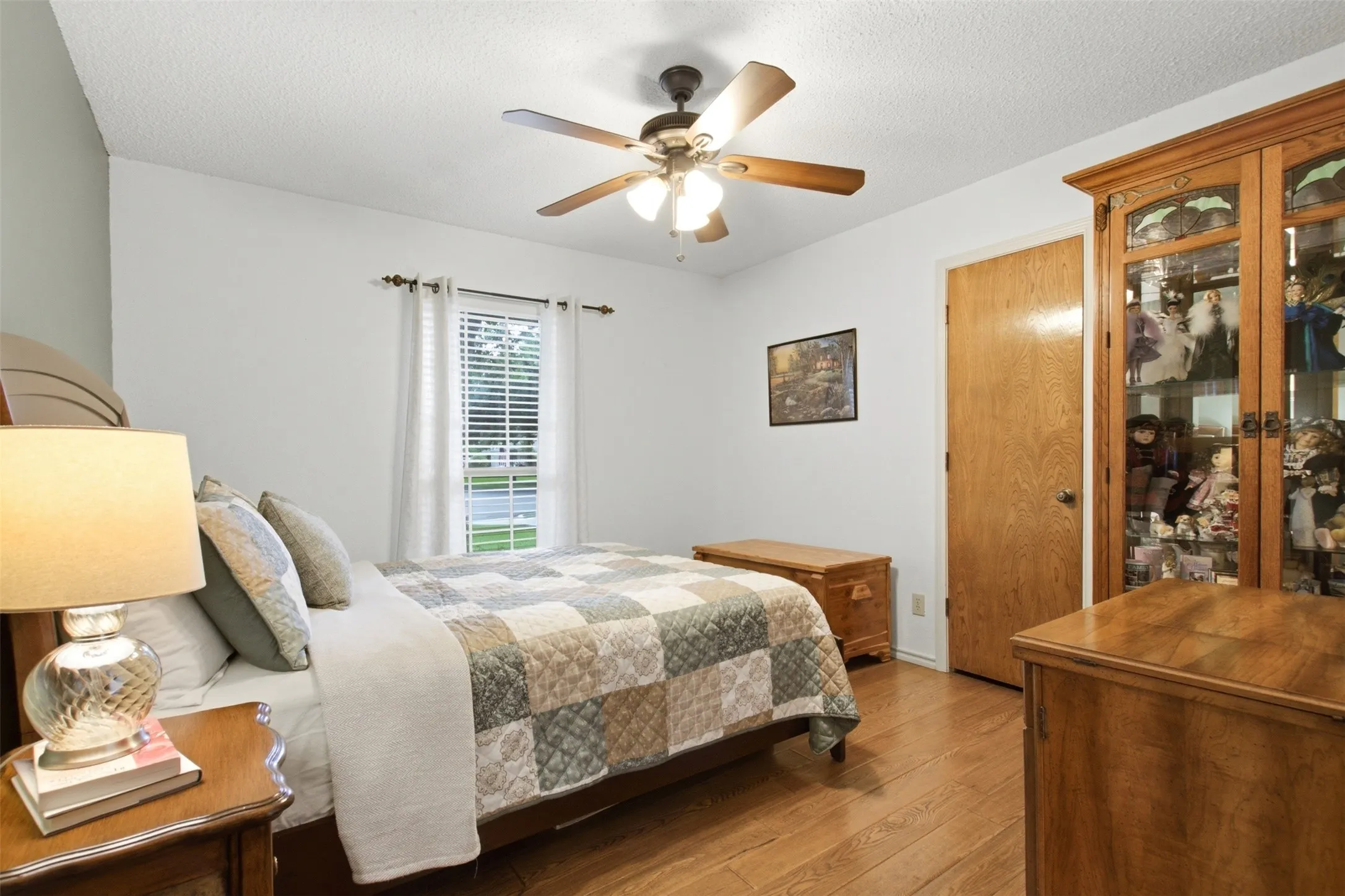 Bedroom featuring wood-finish flooring, a ceiling fan with integrated lighting, a window with horizontal blinds, and a solid wood door