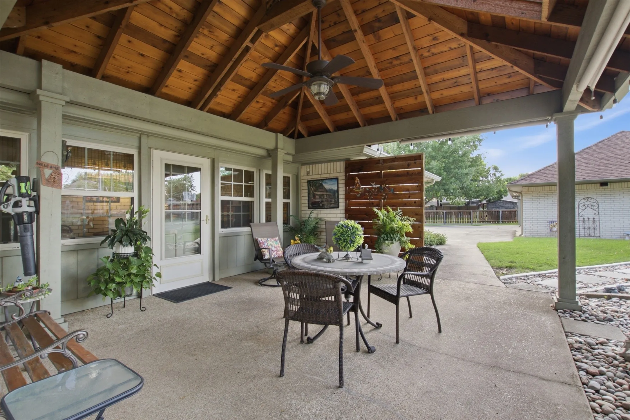 Covered outdoor patio with a vaulted wood-plank ceiling, exposed beams, and a ceiling fan
