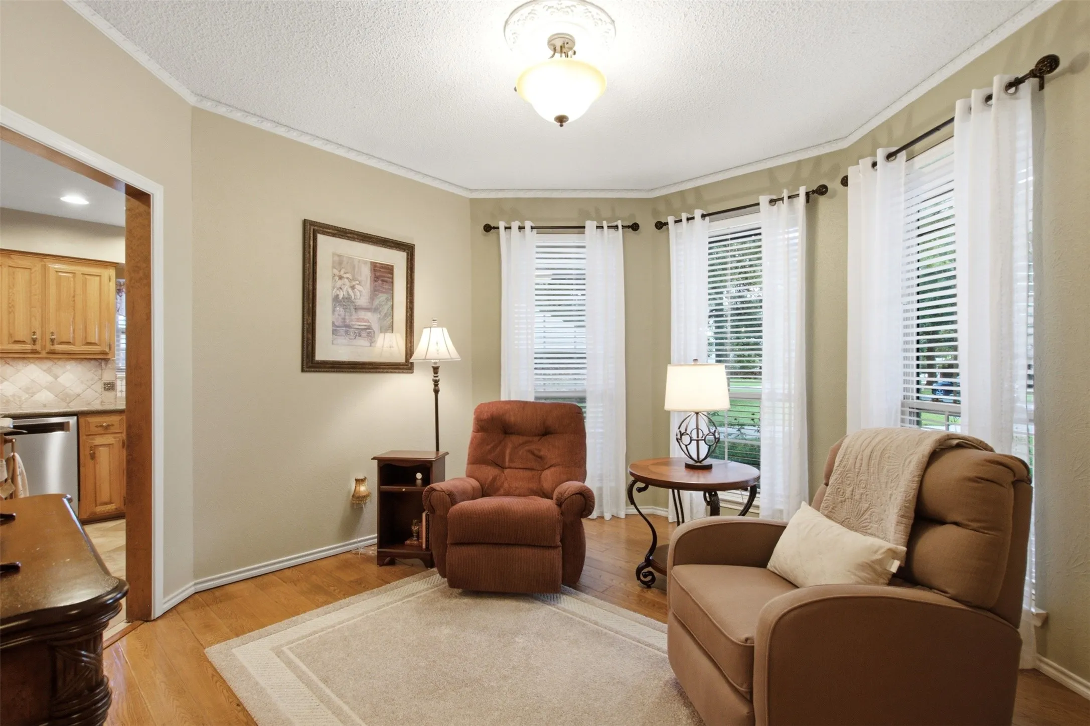 Bay window area featuring multiple tall windows with blinds and sheer curtains, hardwood flooring, and crown molding