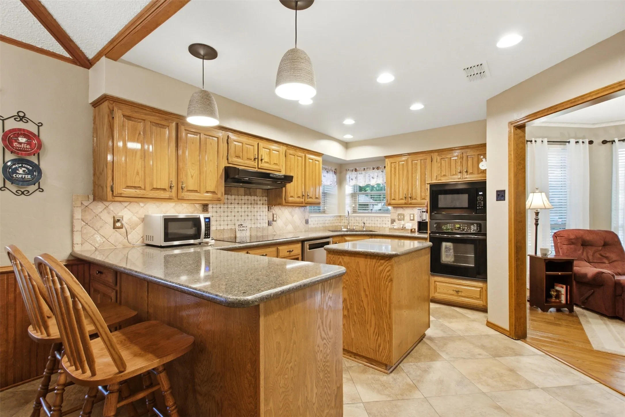 Kitchen featuring light wood cabinetry, granite-style countertops, tile backsplash, built-in double oven, and recessed lighting