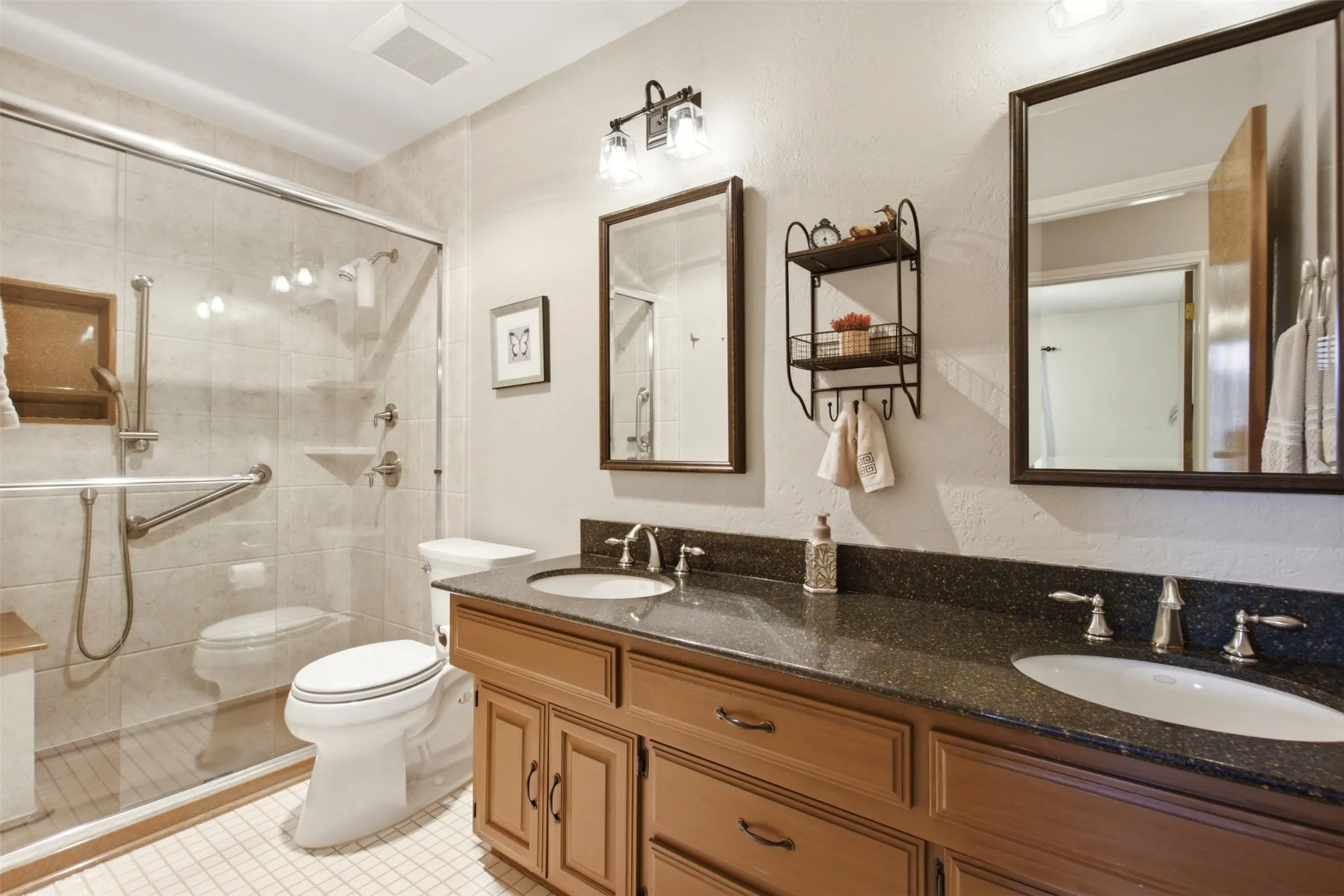 Dual vanity with dark stone countertop, undermount sinks, and wood-finish cabinetry